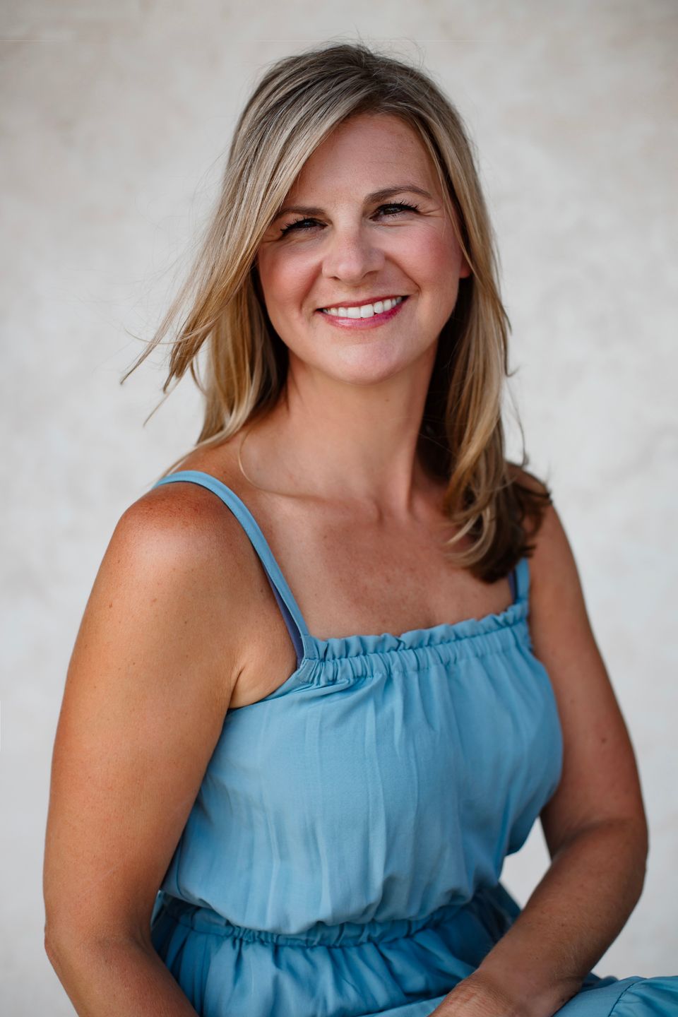 Professional headshot of person in light blue dress smiling against neutral background.