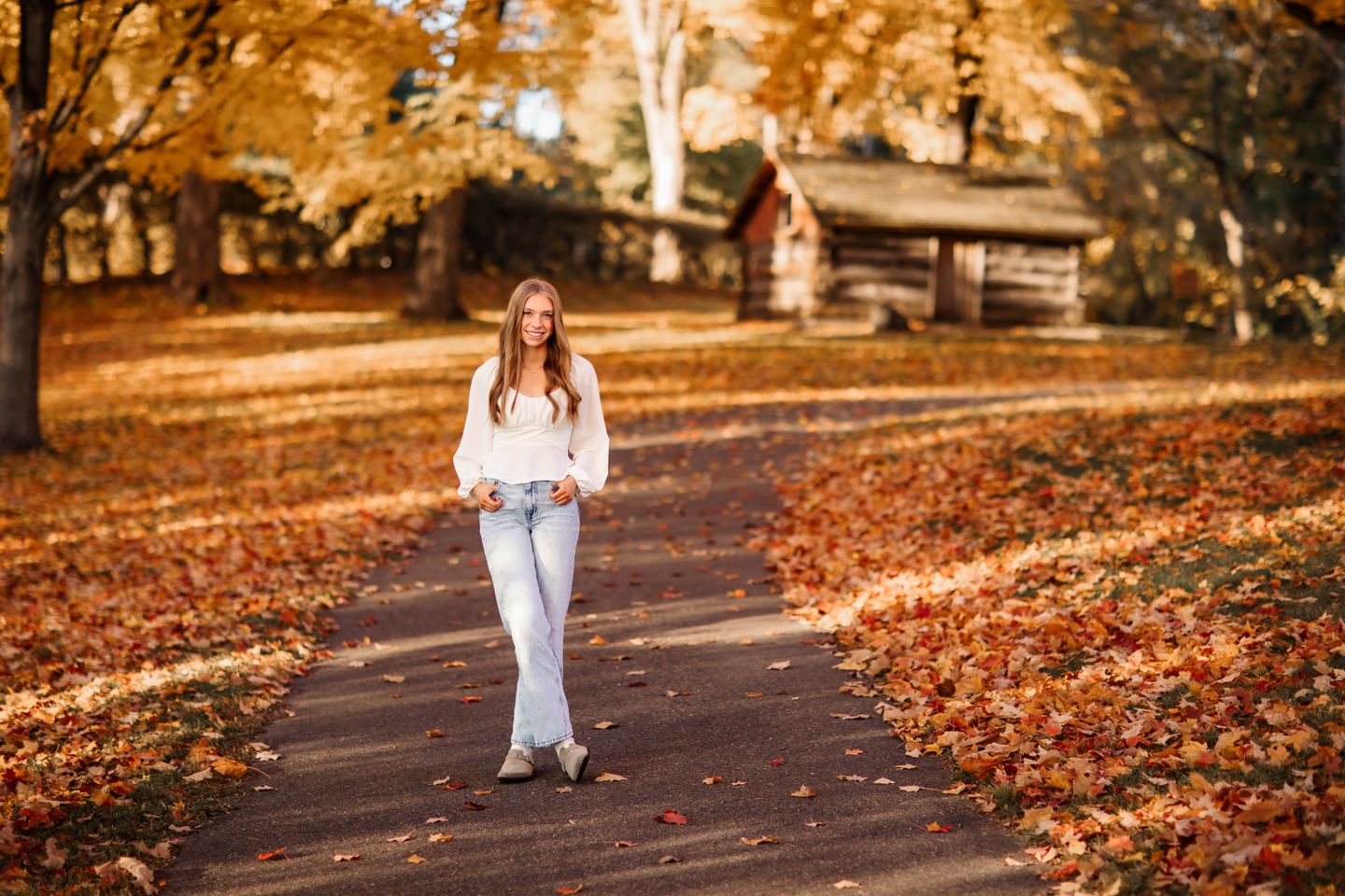 Person walking along an autumn path with fallen orange leaves and trees.