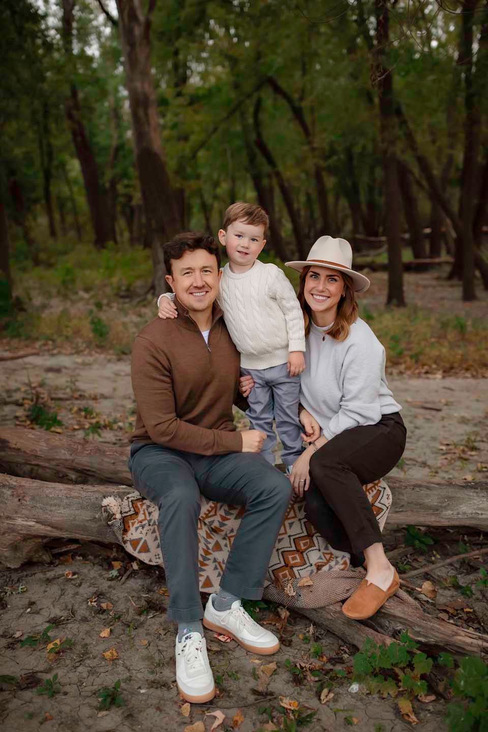 A family sits together on a fallen log in a scenic wooded area.