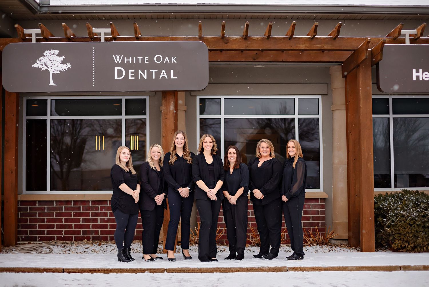 Medical staff poses together in front of White Oak Dental office exterior with wooden pergola and brick facade.