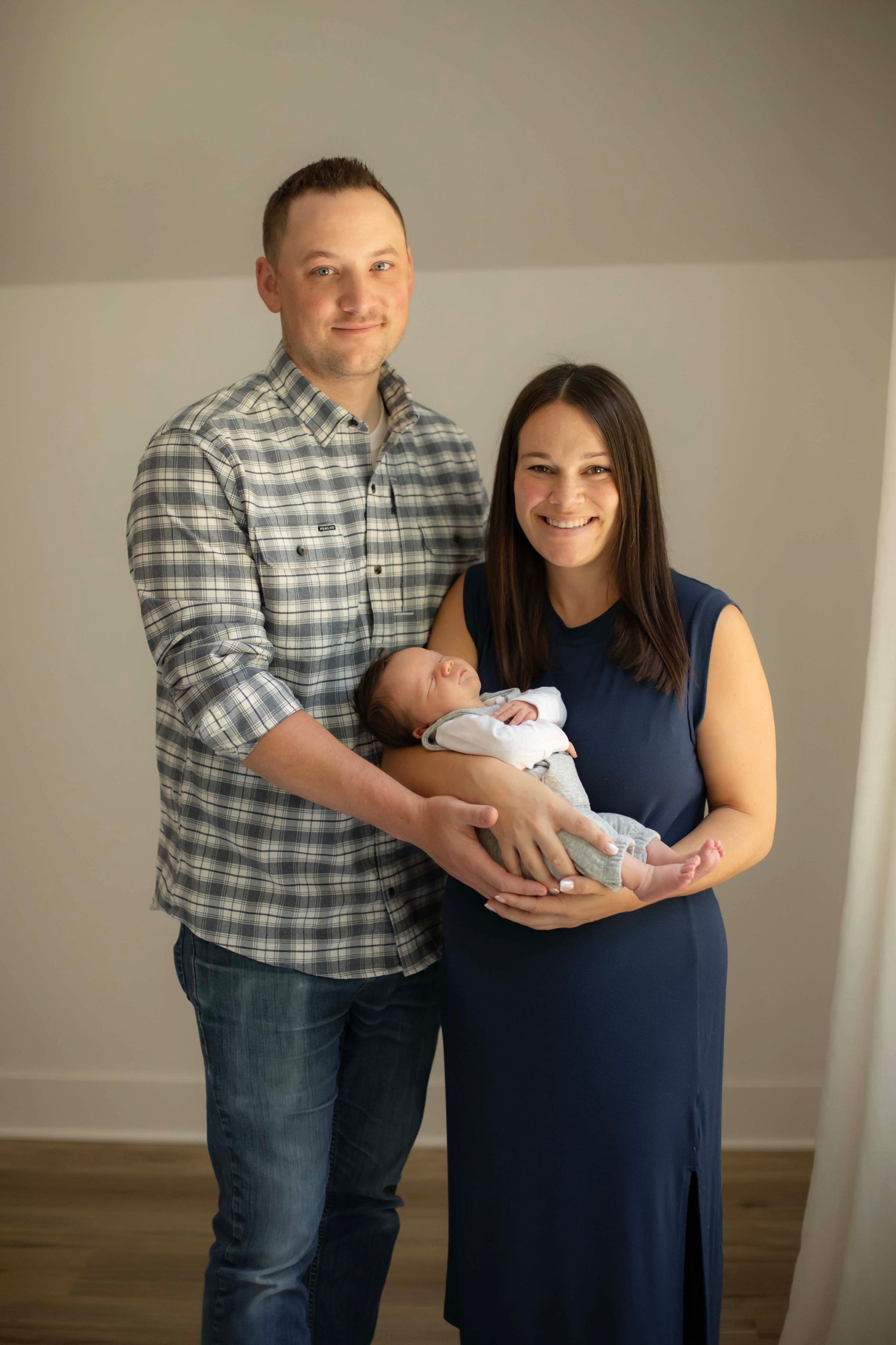 Happy couple smiling and holding their newborn baby during an indoor family portrait session.