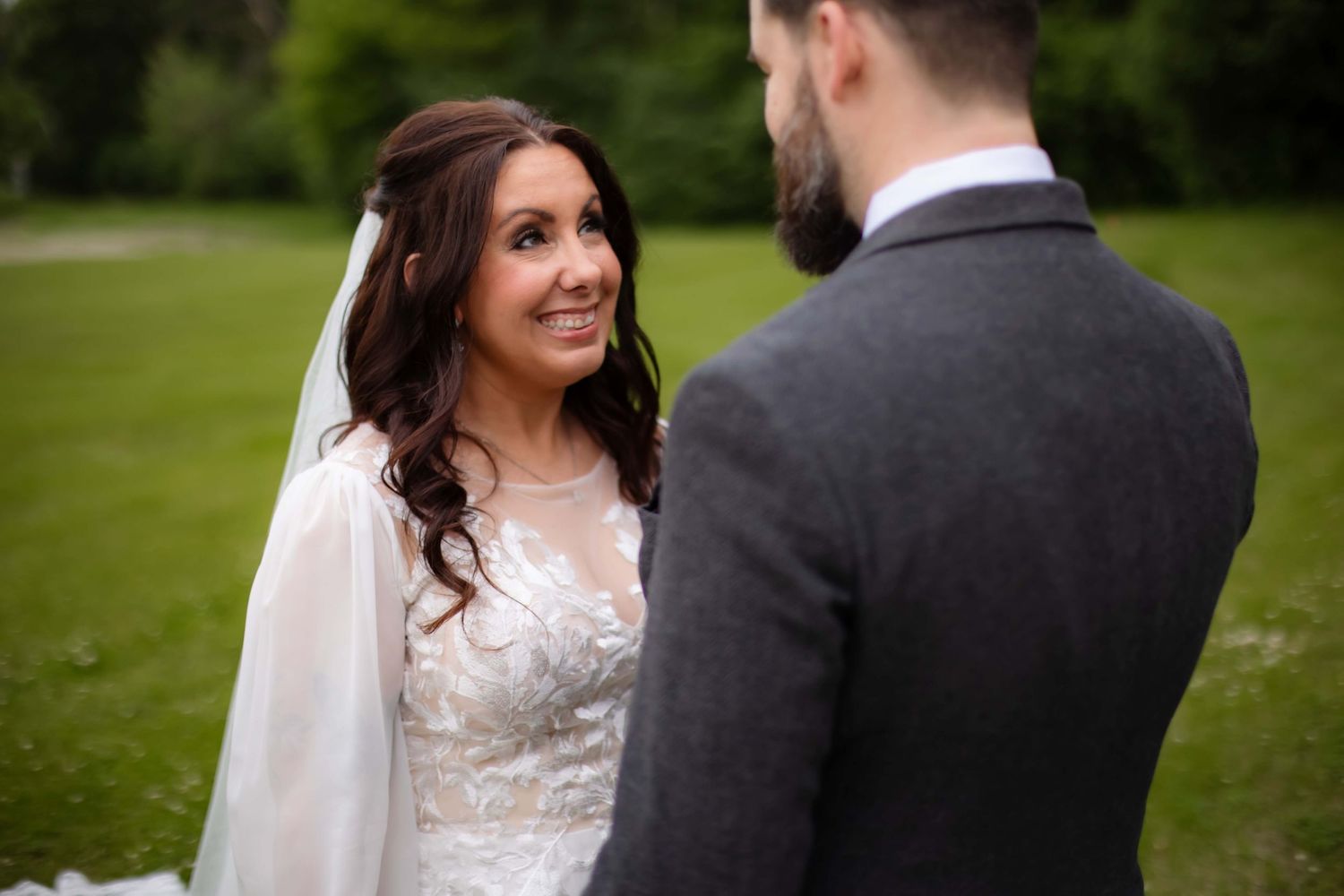 Couple in wedding attire standing together on lush green grass during an outdoor ceremony.