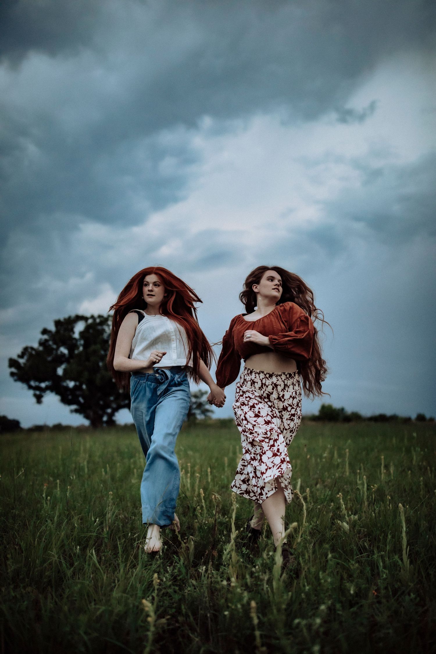 Two figures in casual outfits dance and move through a windswept field at dusk.