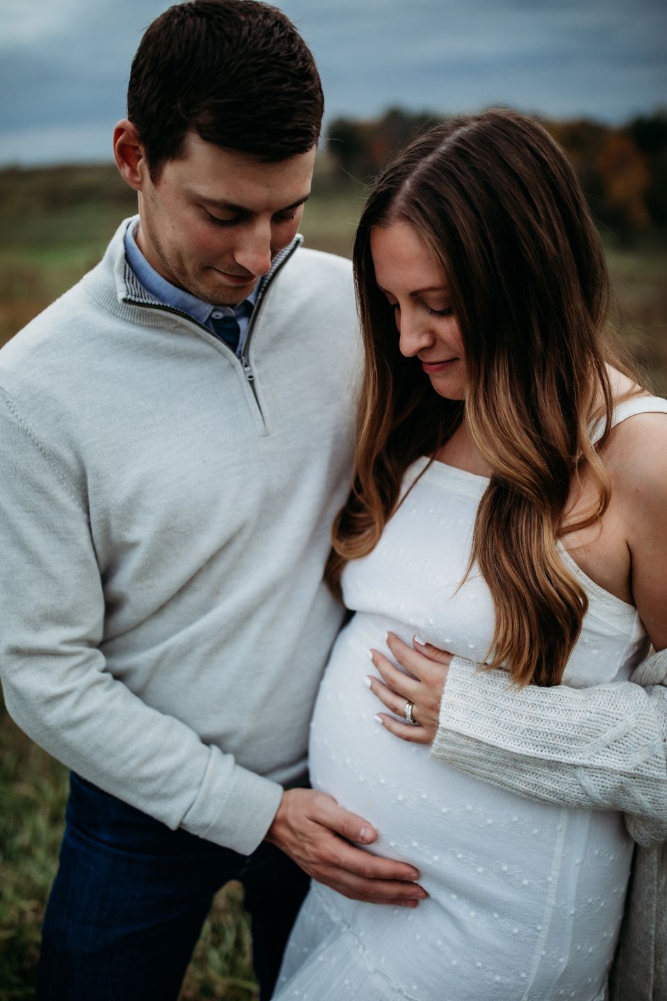 Intimate couple in white outfits embrace while expecting a baby in an outdoor autumn setting.