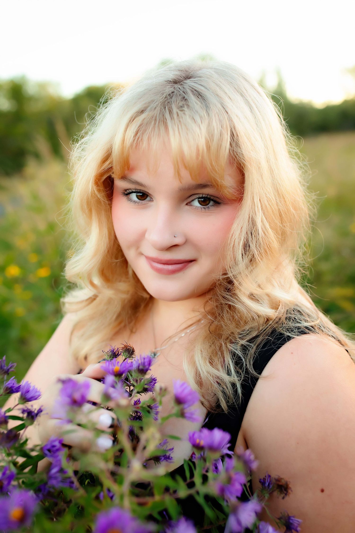 Portrait in a field of purple wildflowers during golden hour showing blonde wavy hair and natural lighting.