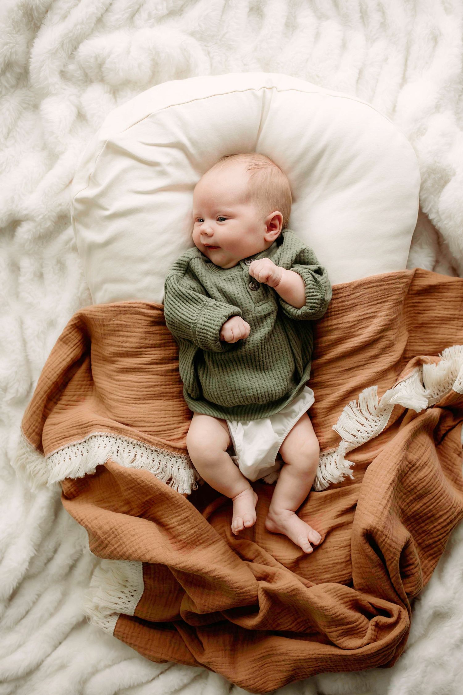 Baby in sage green sweater lying on textured blankets with peaceful expression.