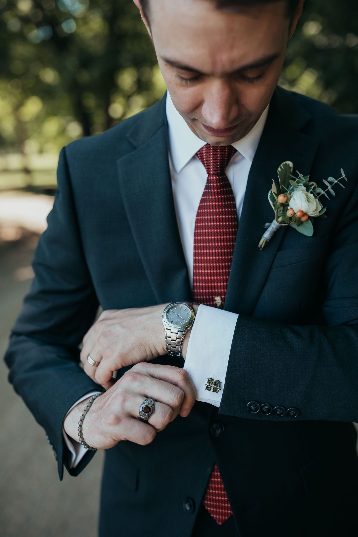 Close-up of formal attire showing watch, cufflinks, boutonniere and red tie details.