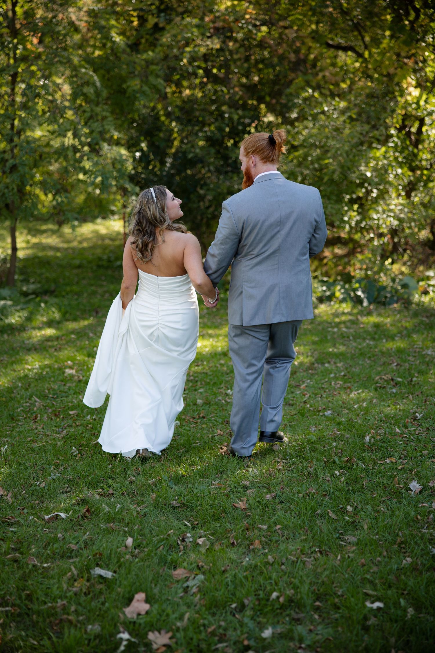 A couple in wedding attire walks hand in hand through a lush garden setting on their special day.