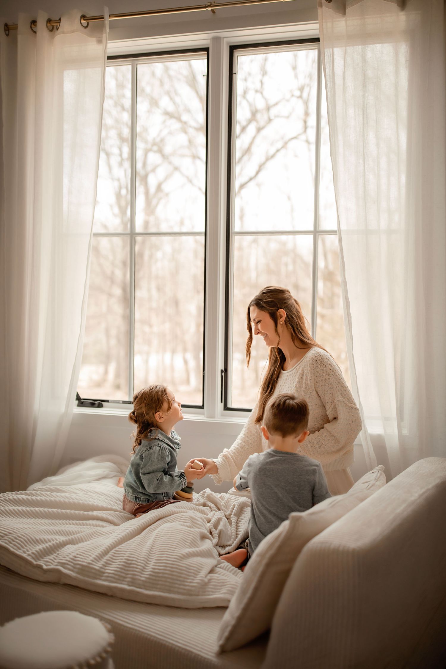 A tender moment shared between family members on a bright white bed near large windows.