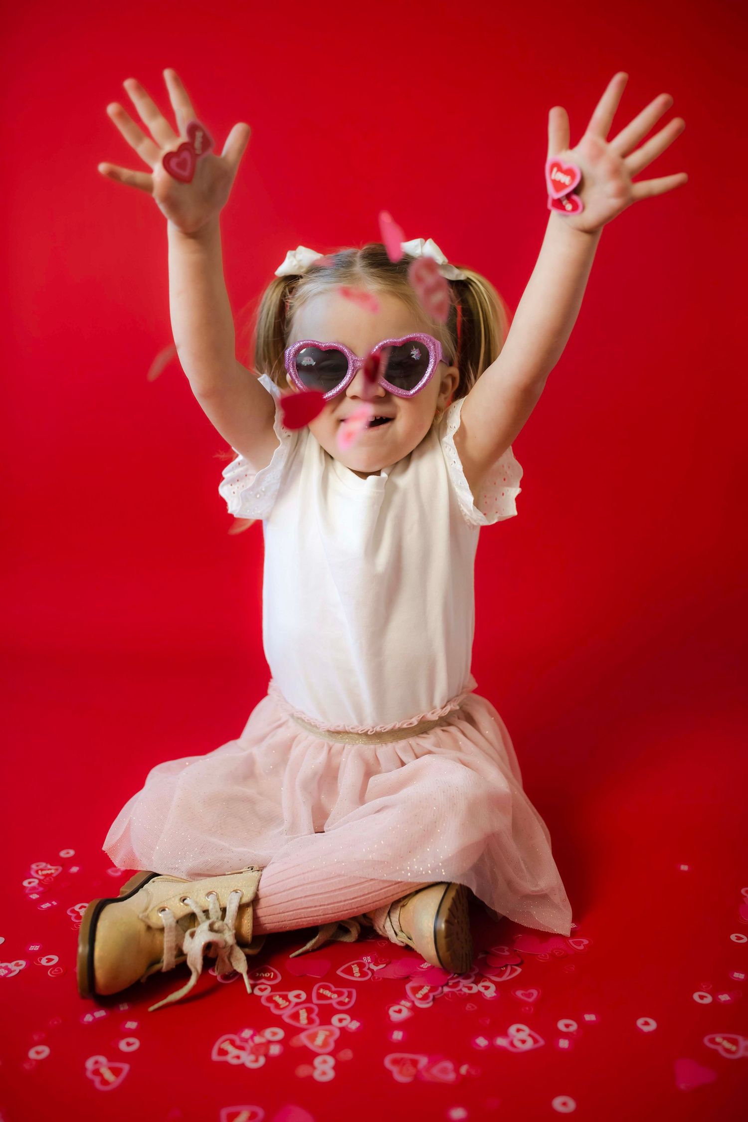 Joyful pose against red background wearing pink tulle skirt and heart sunglasses.