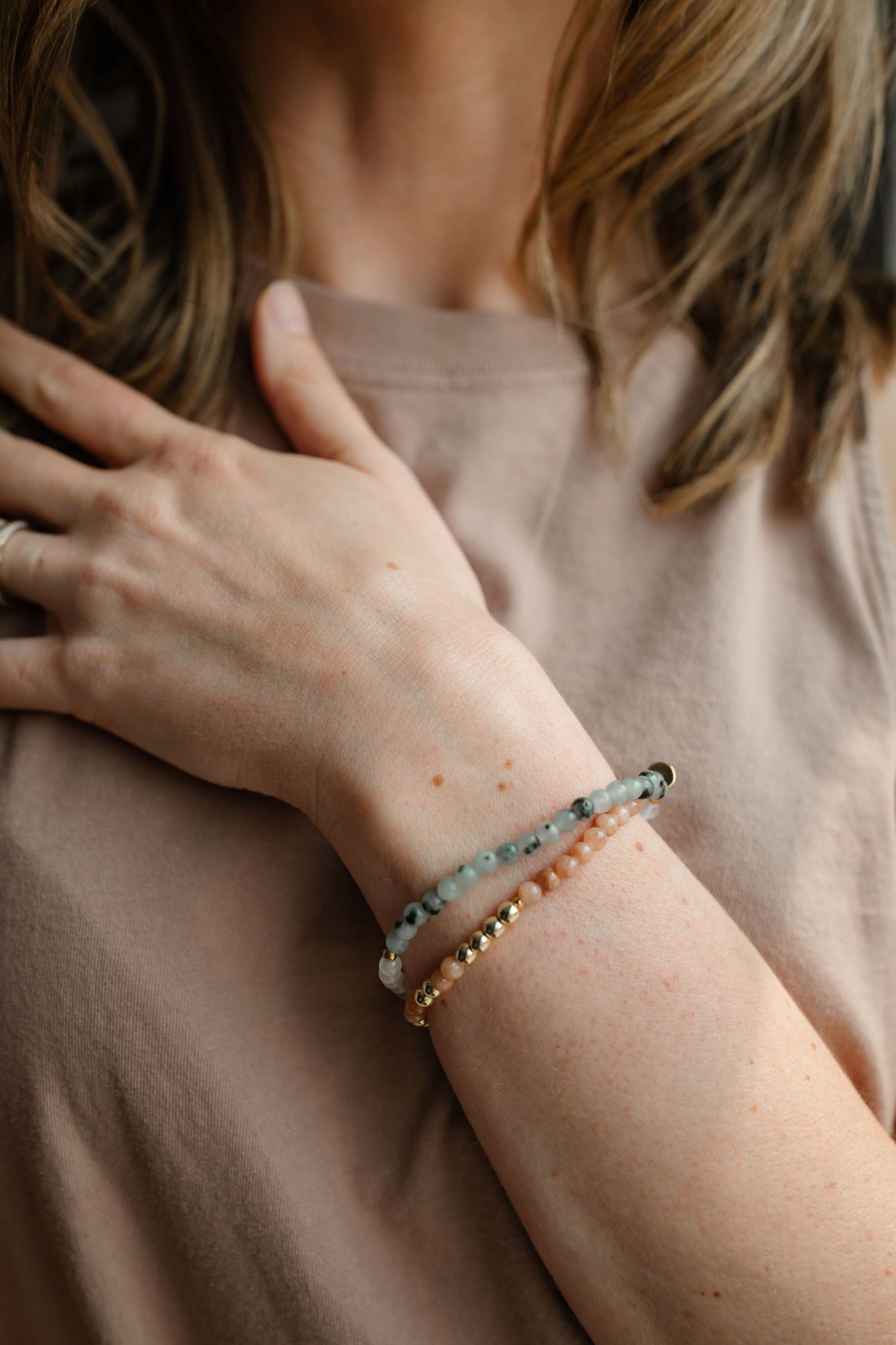 Close-up of delicate beaded bracelets on wrist against neutral beige sweater.