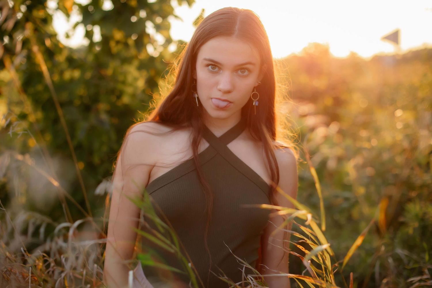 Dramatic sunset portrait in black crossover top against golden backlit grass.