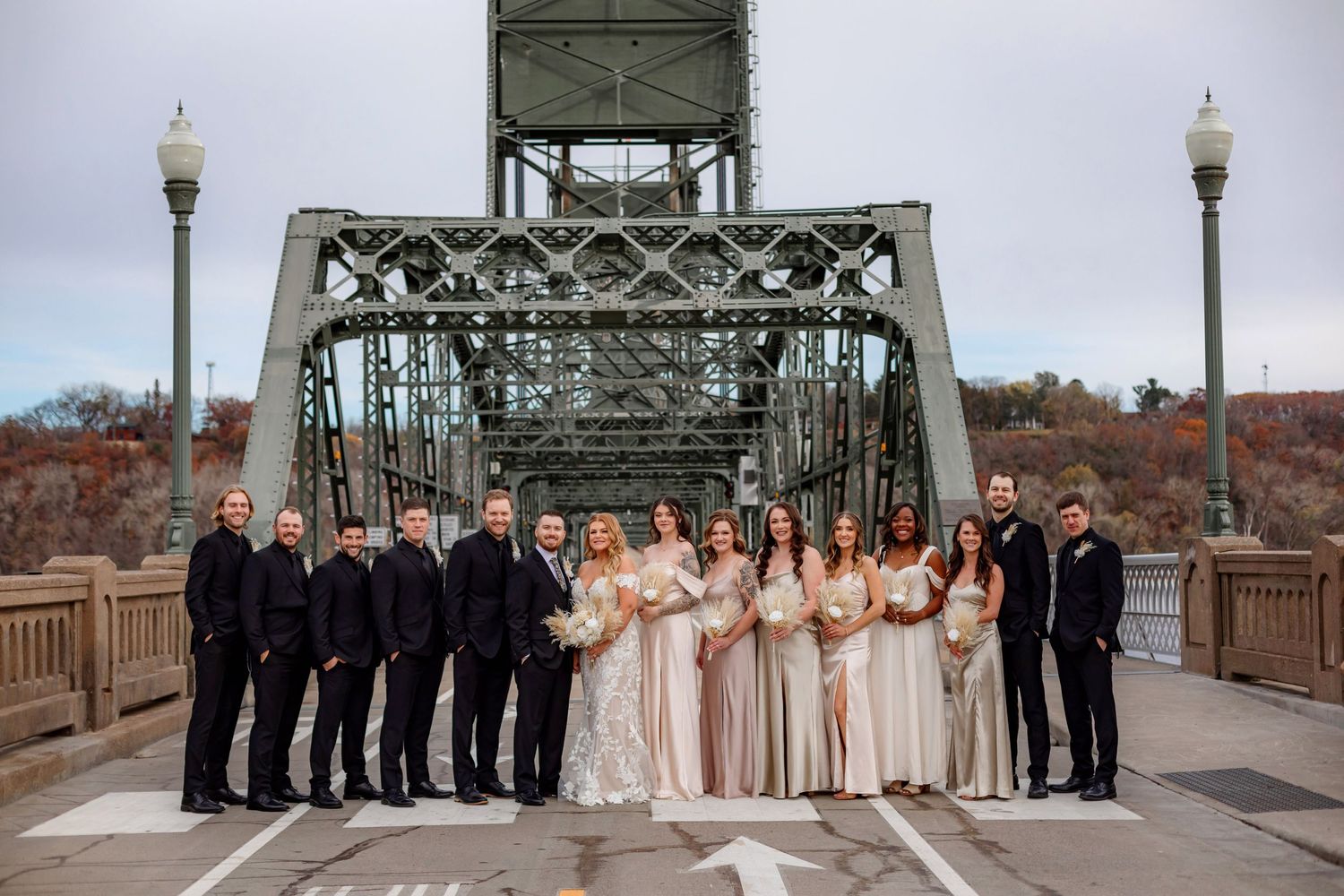 Wedding party in black suits and neutral dresses lined up formally on bridge.