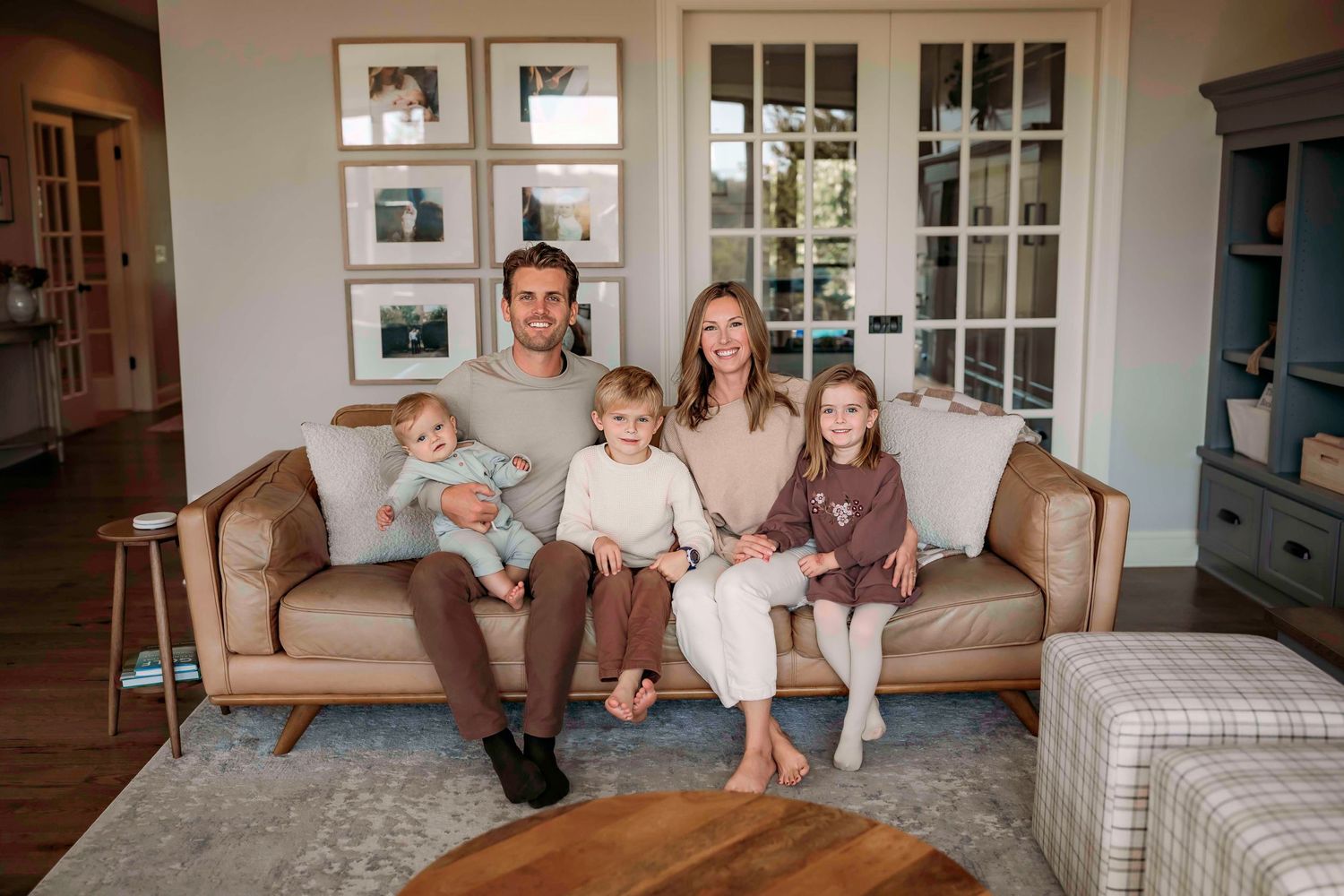 A family sits together on a brown leather couch in their cozy living room.