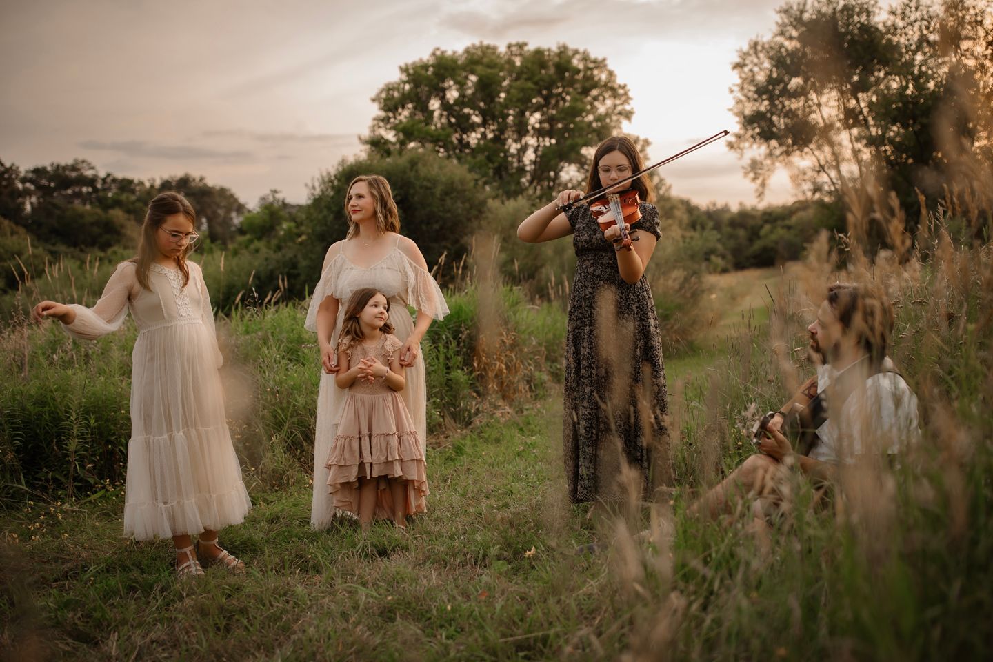 Group wearing light flowy dresses pose together in a wild grass field at sunset.