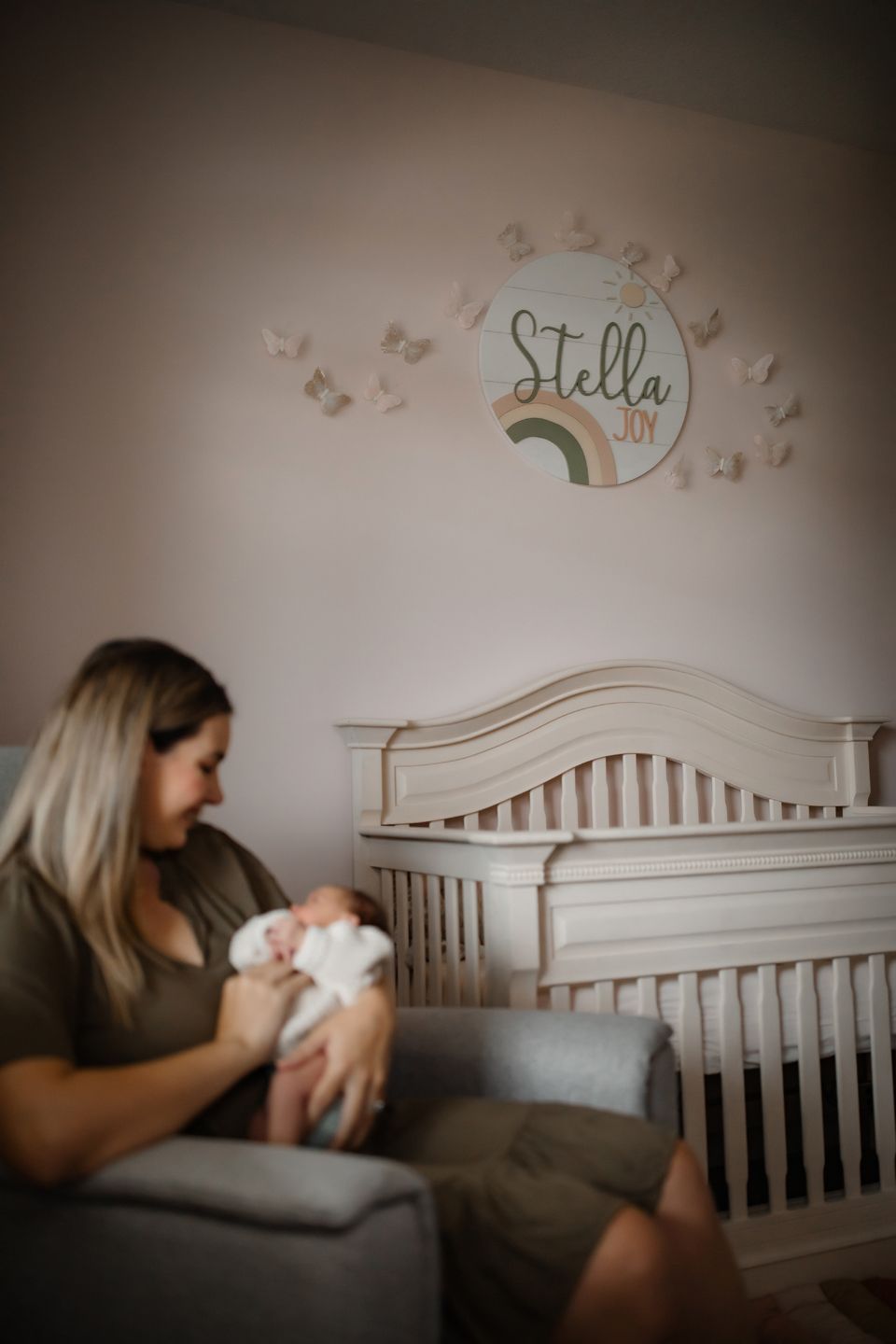 A nursery with soft decor featuring a crib, rocking chair, and wall art with butterflies and rainbows.