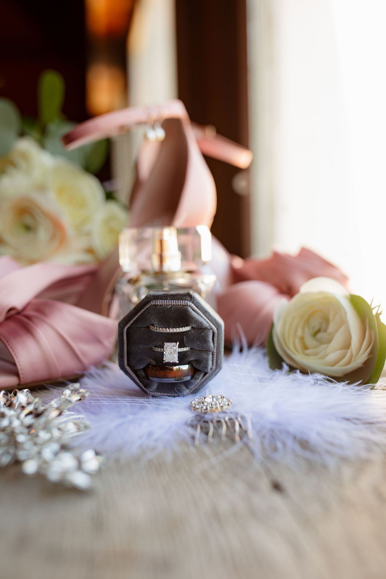 Wedding rings and pink ribbons arranged on delicate white lace with soft roses creating an elegant bridal detail shot.