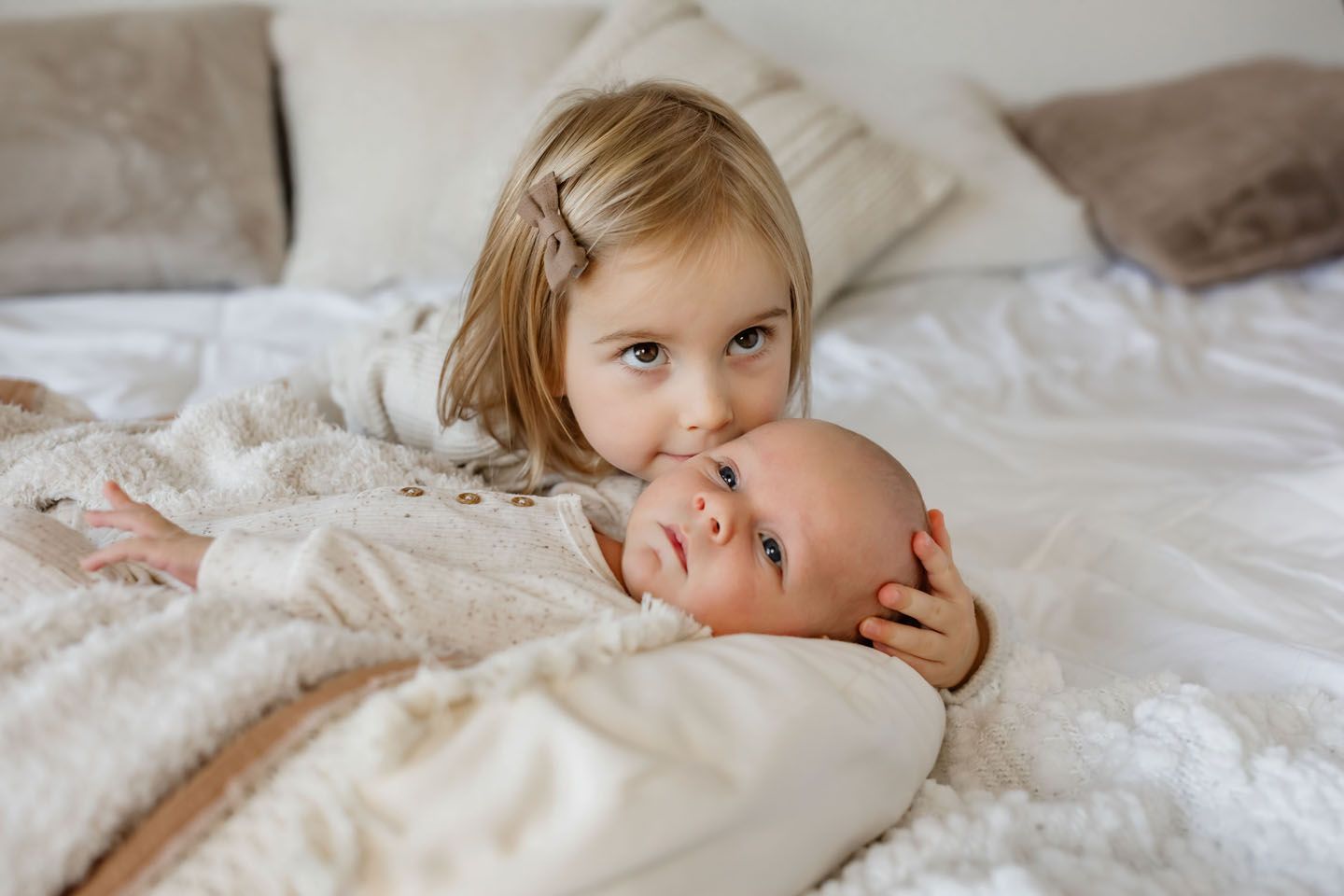 Sweet tender moment between siblings on white bedding.