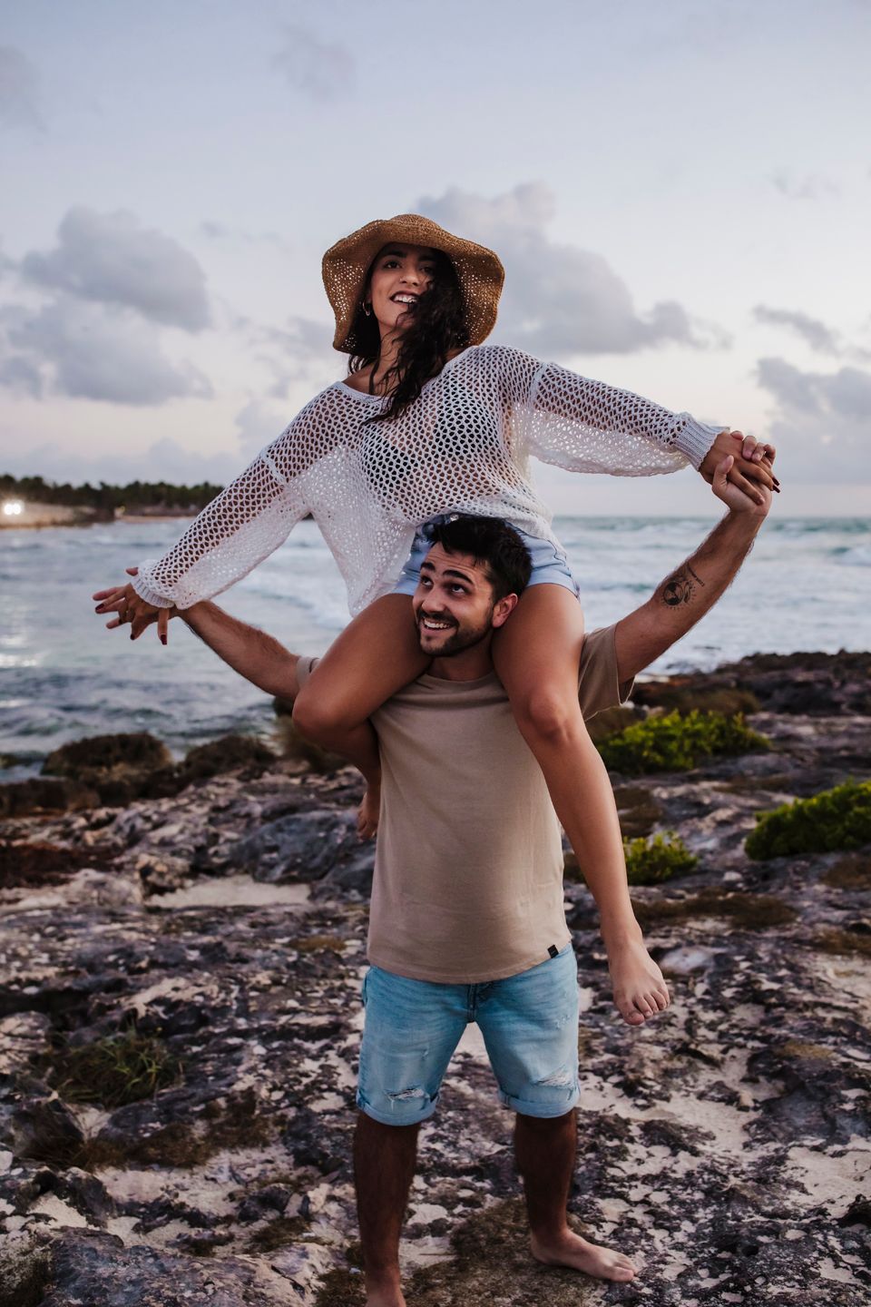 Playful couple having fun on coastal rocks with ocean waves in background.