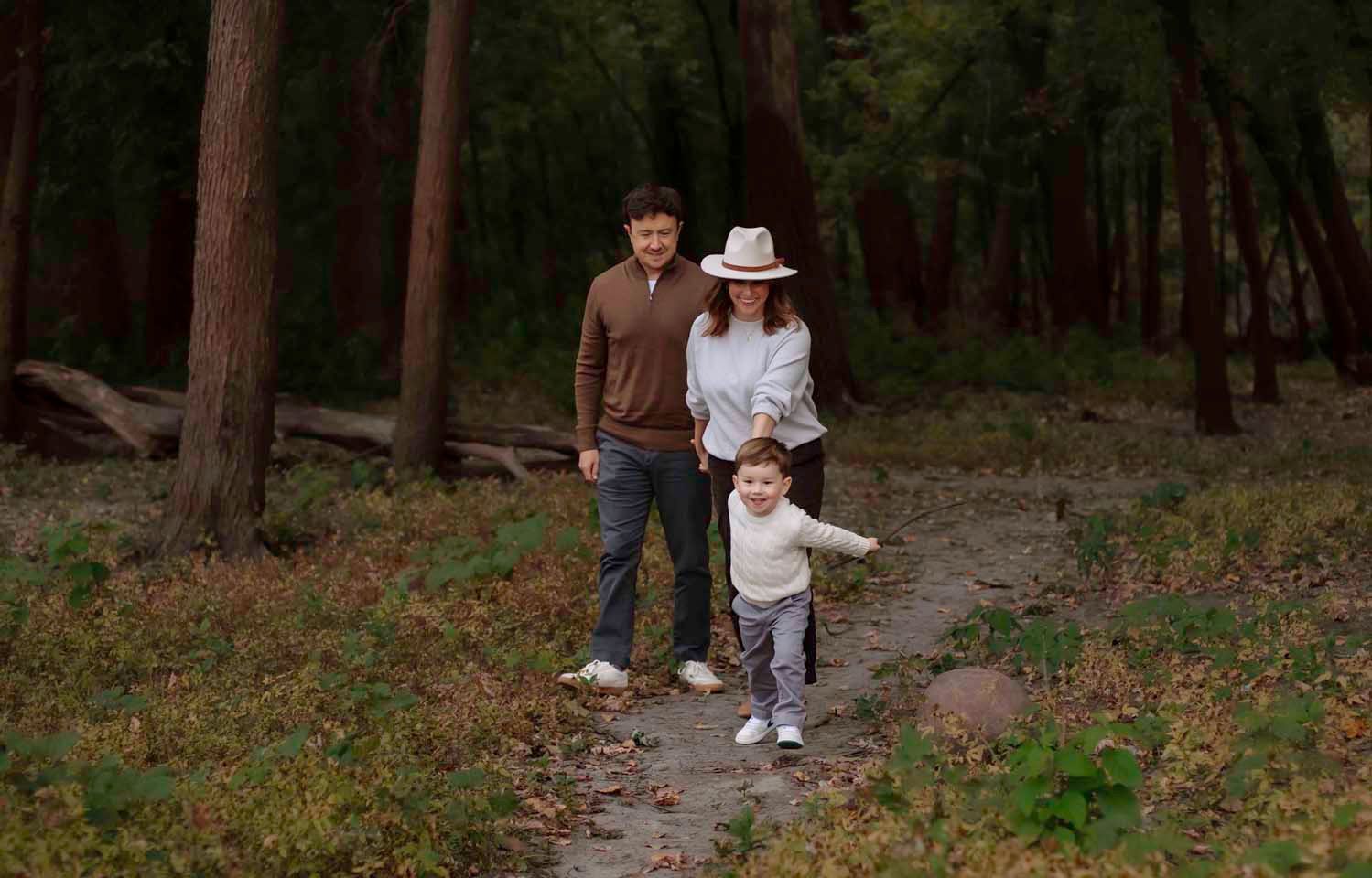 Family walking together down a forest trail surrounded by tall pine trees on an autumn afternoon.