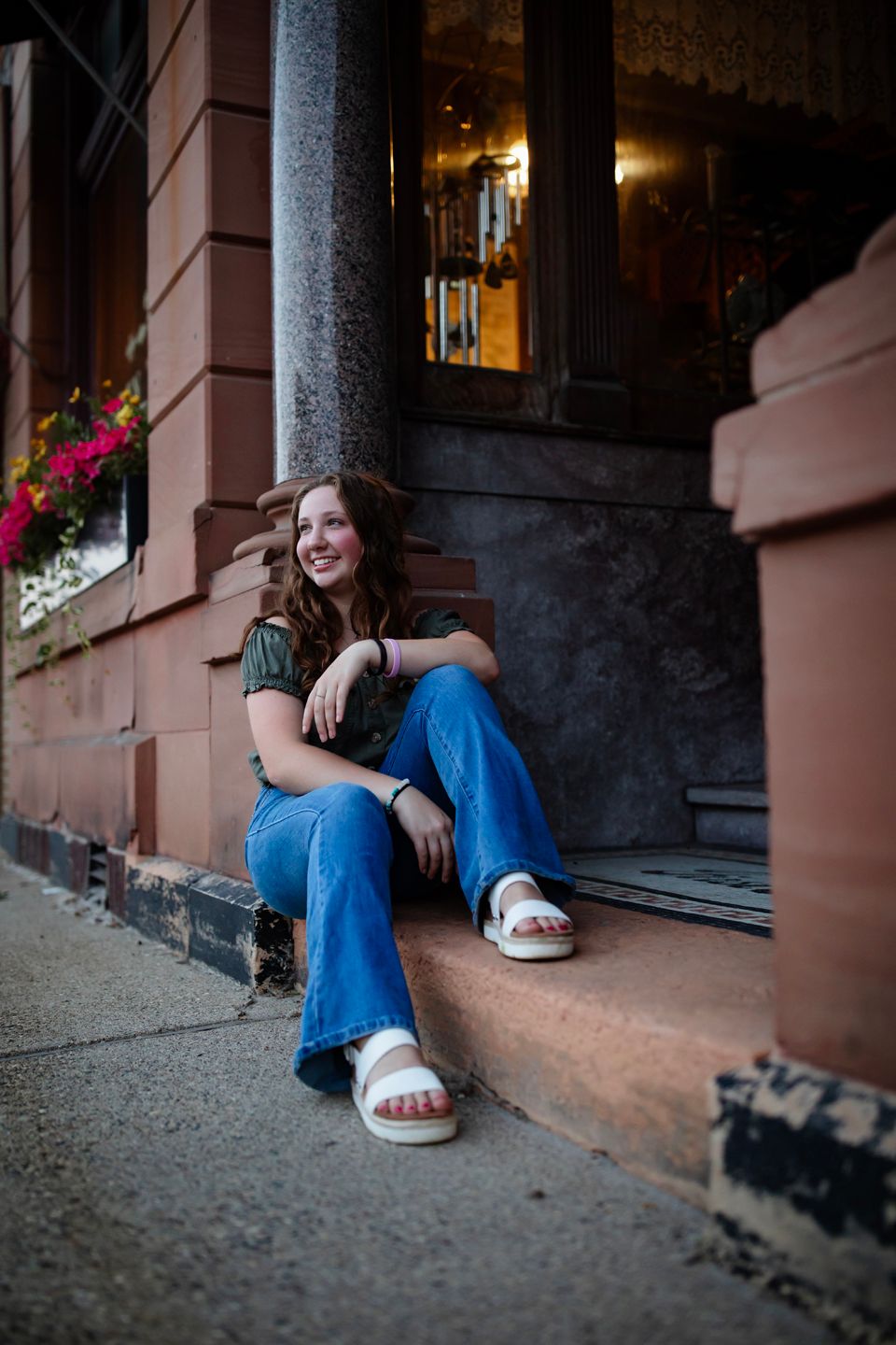 Person in casual wear sitting on urban steps with flowers nearby.
