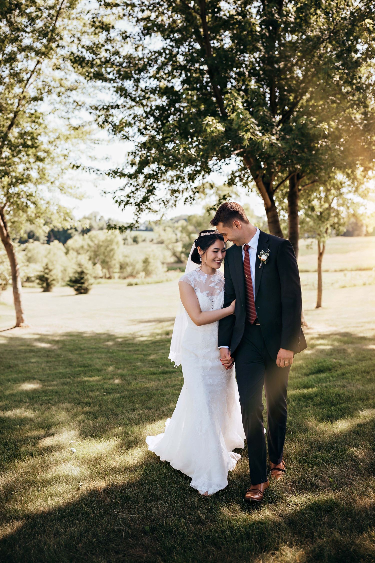 Wedding couple walking together on sunny lawn with trees in background.