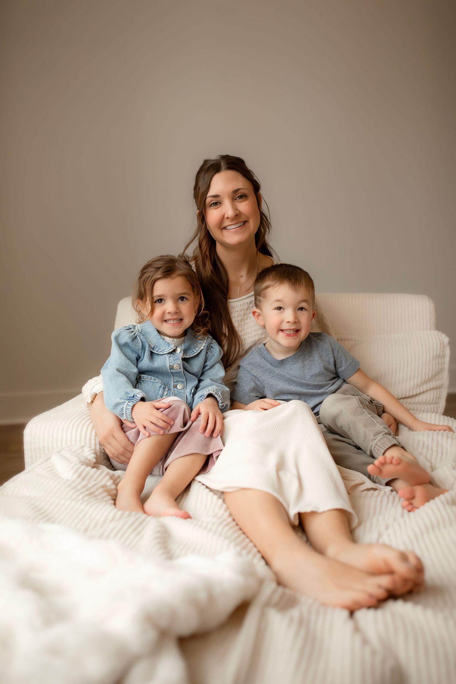 Two children wearing blue shirts relax together on white bedding in a cozy bedroom setting.