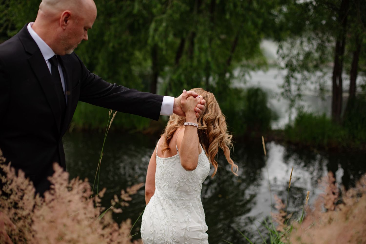 A romantic outdoor wedding photoshoot with a couple embracing among tall grasses and trees in a natural setting.