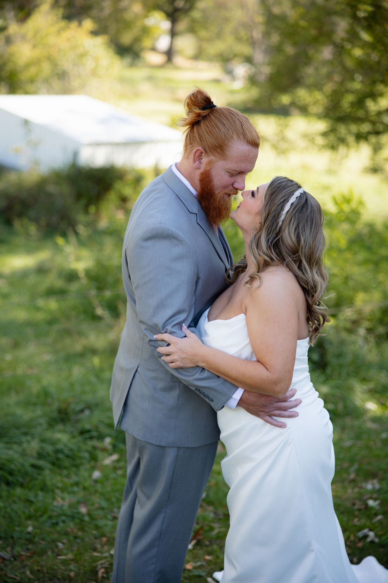 Romantic outdoor wedding moment between couple in grey suit and white dress surrounded by greenery.