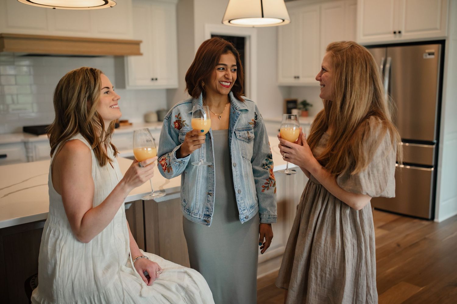Three friends enjoying drinks and conversation in a modern white kitchen.