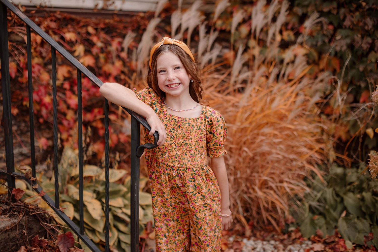 Autumn portrait with rust-colored dress in front of red fall foliage and ornamental grasses.