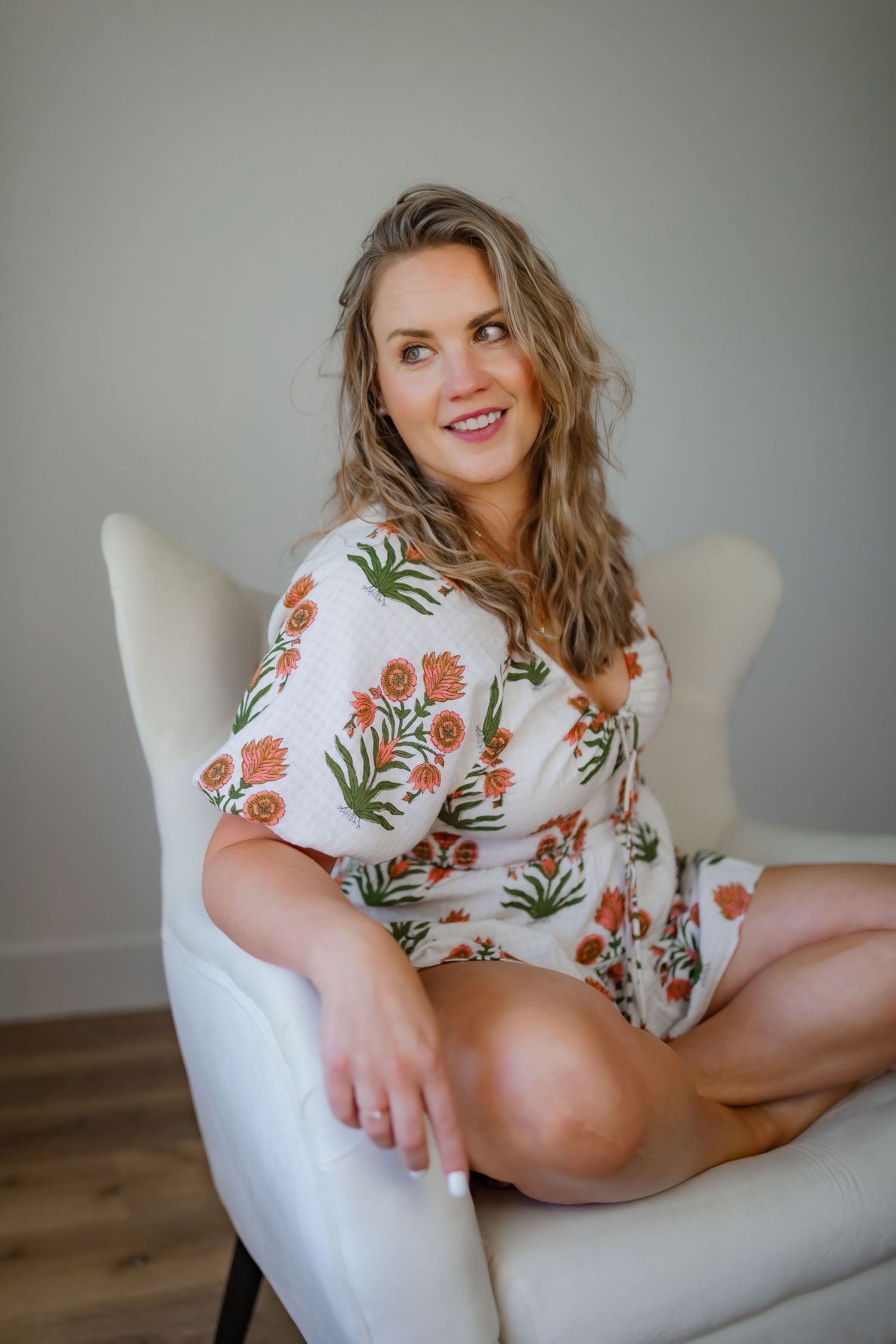 Floral romper with orange botanical print while relaxing in white armchair.