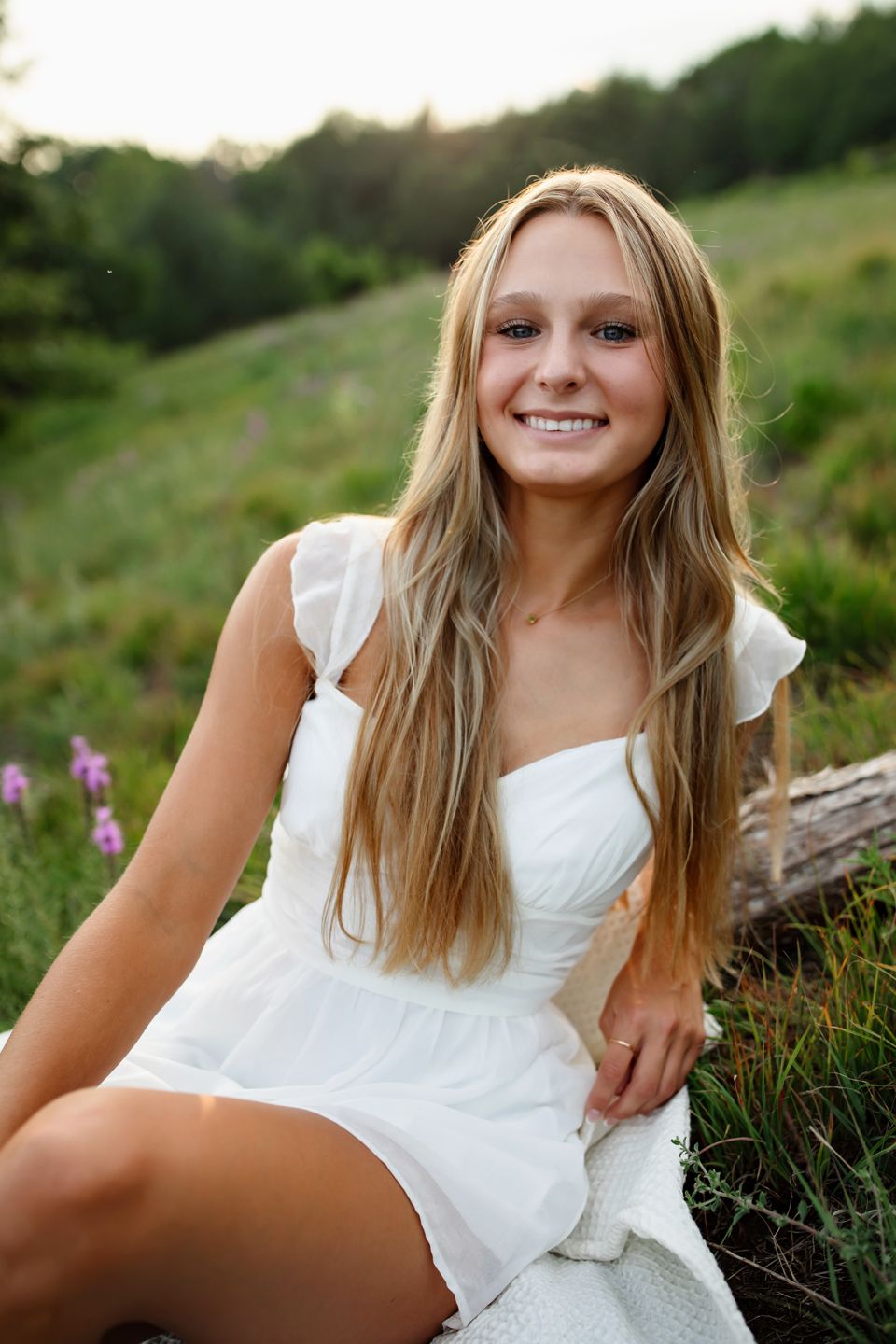 Someone wearing a white sundress sitting outdoors among wildflowers.