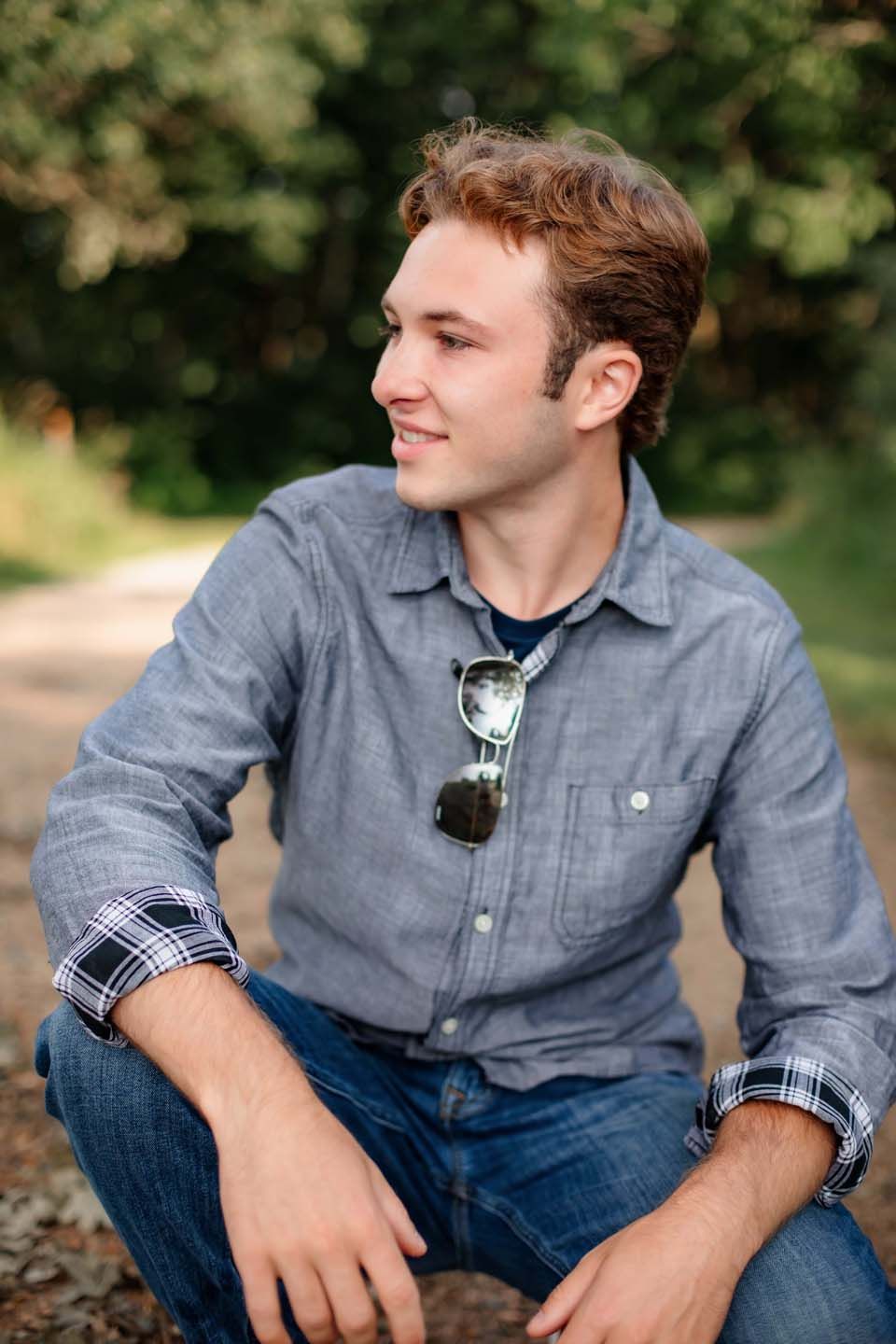 Casual outdoor portrait with sunglasses hanging on blue button-down shirt collar.