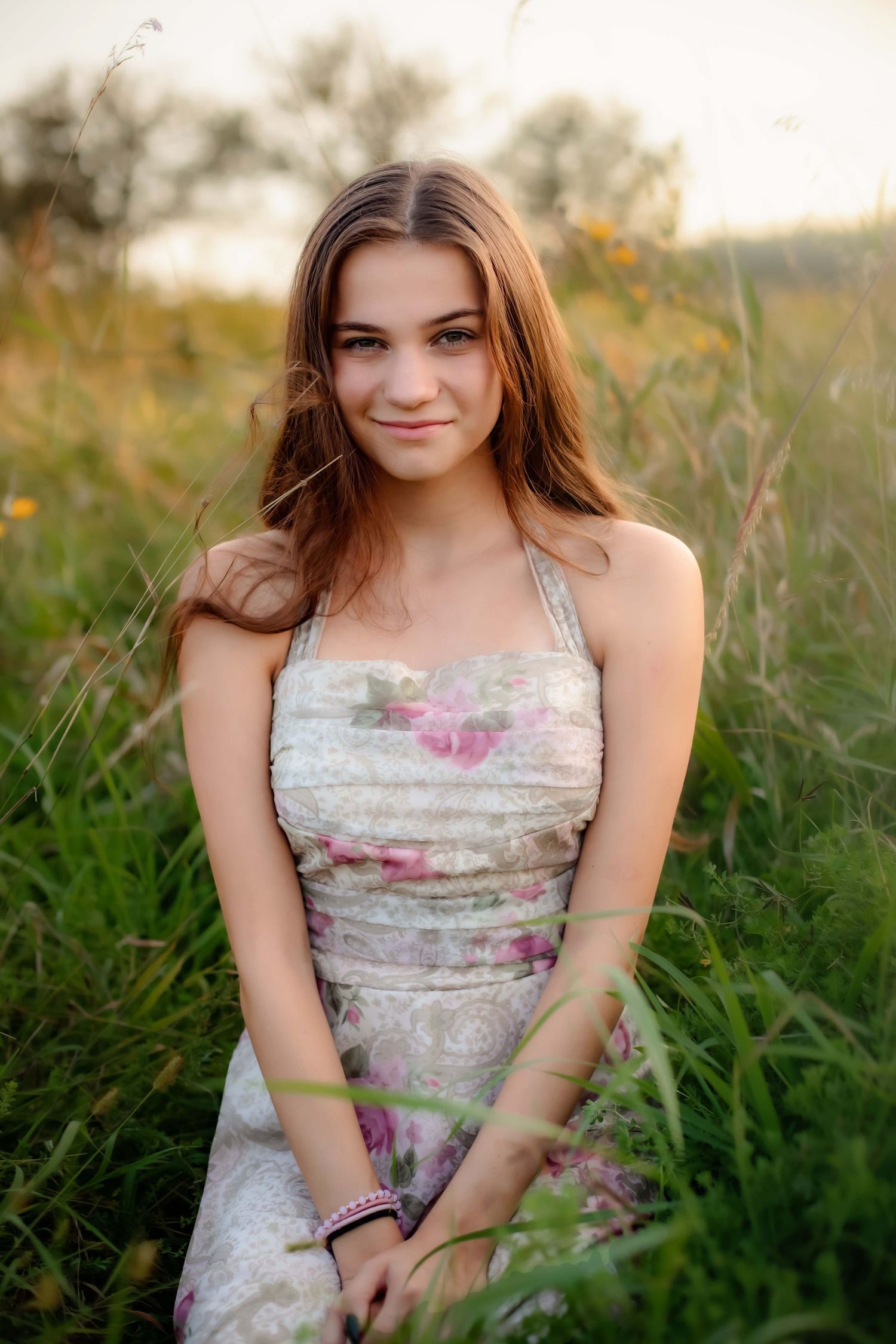 Summer portrait in floral sundress sitting among wild grasses at sunset.