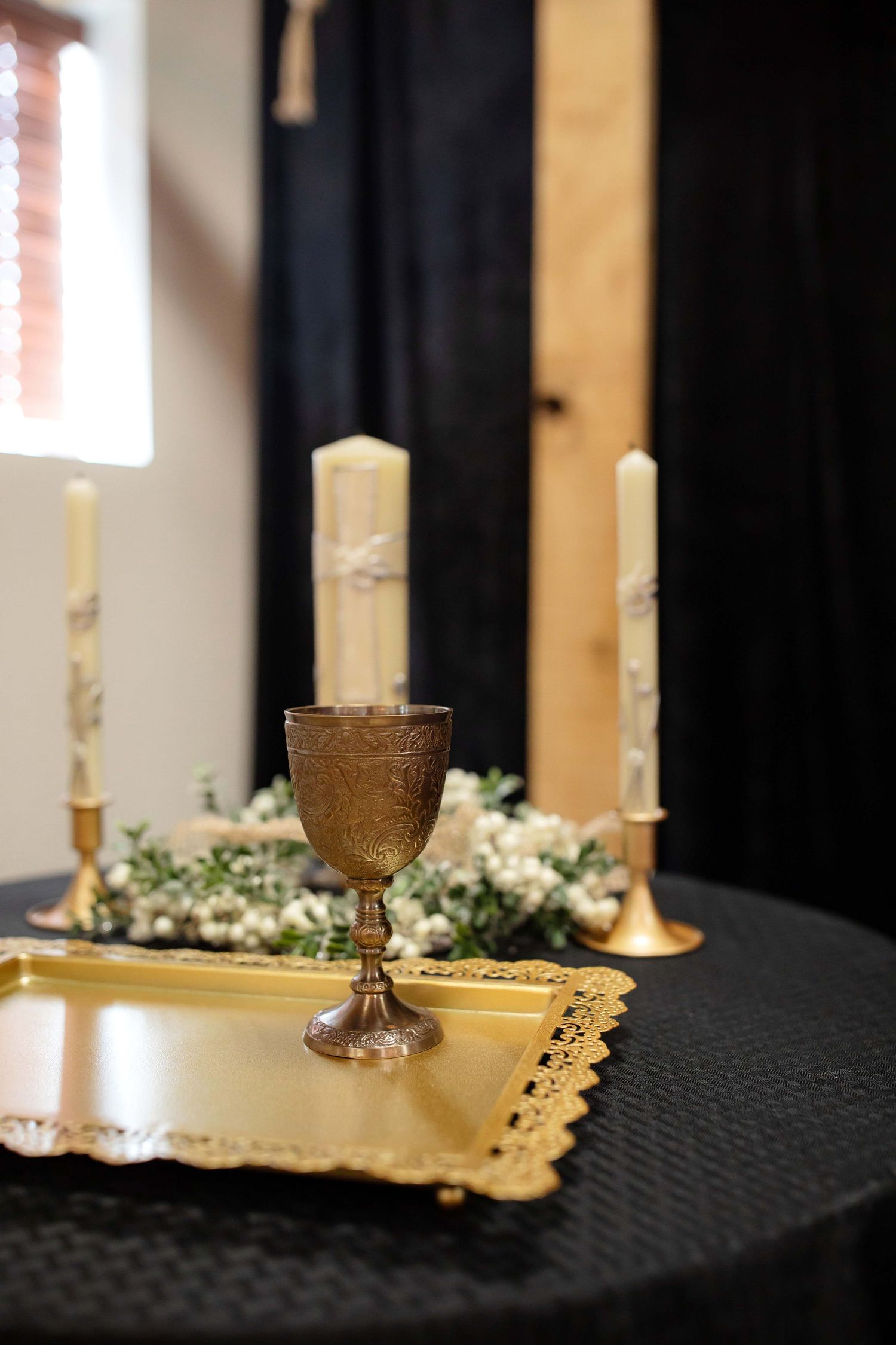 White candles and delicate floral arrangements adorn a dark tablecloth at an elegant wedding reception.