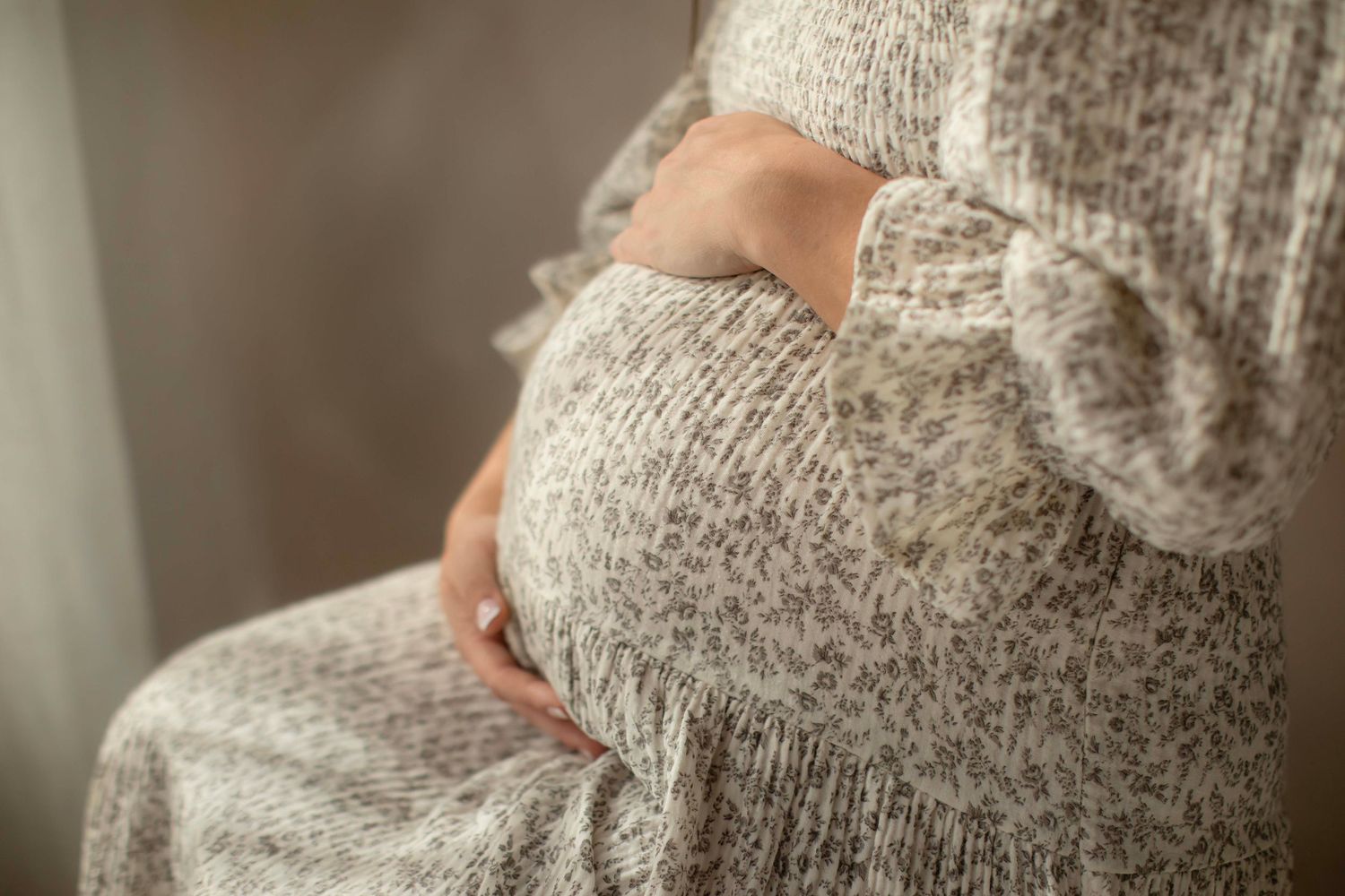 Pregnant woman in floral dress gently cradling her baby bump while sitting, maternity photography concept.