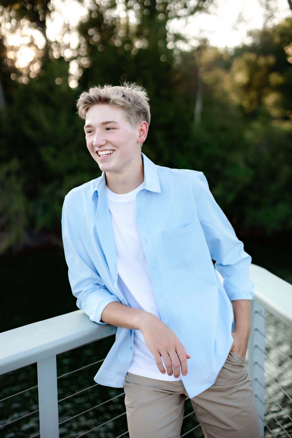 Casual waterfront portrait at golden hour wearing light blue button-down shirt.