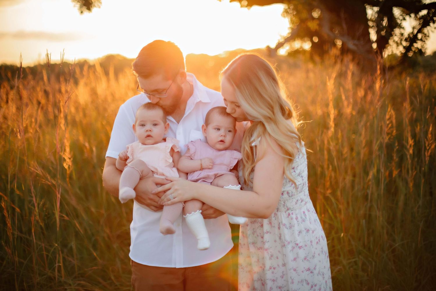 A family shares a tender moment with their twins in a sun-drenched field.