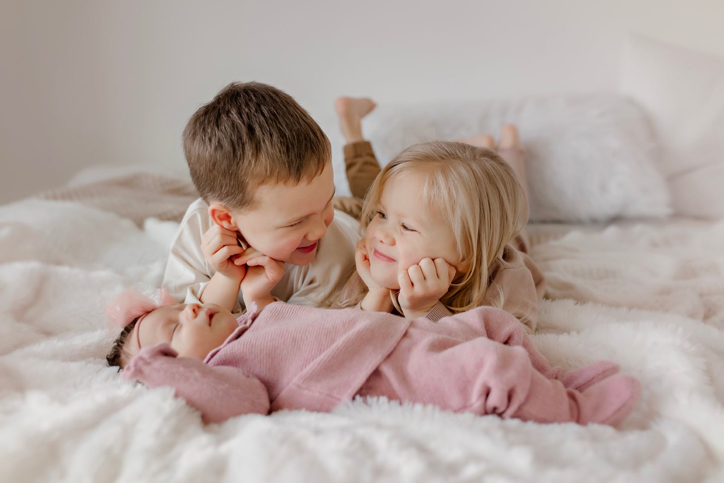 Two young children lying on white bedding share a sweet moment together while dressed in cozy sleepwear.