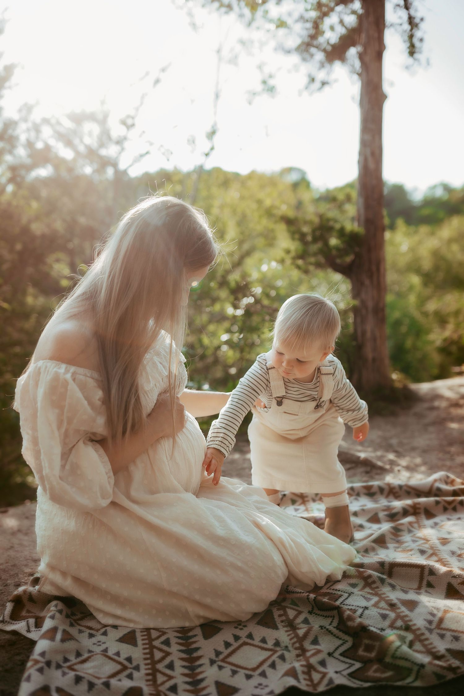 A gentle moment shared on a patterned blanket in dappled forest sunlight.