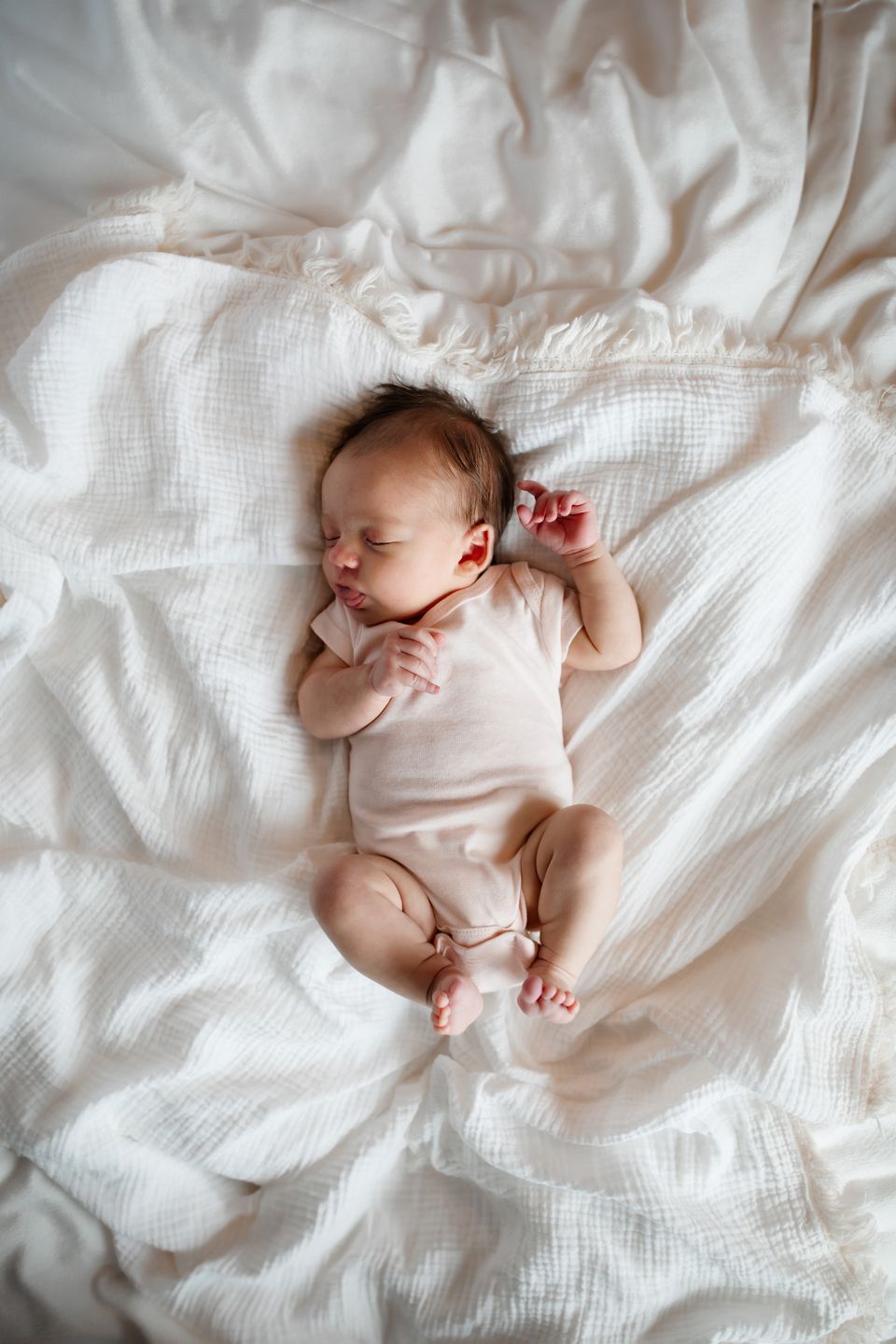 Peaceful newborn sleeping in white onesie on textured white bedding.