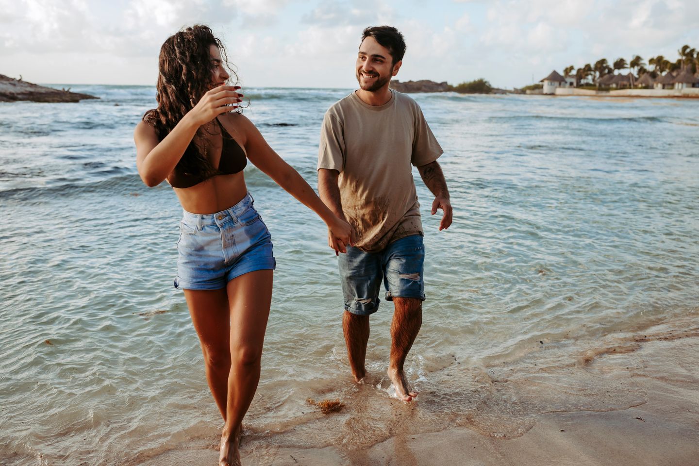 A couple splashing through shallow ocean water while holding hands at sunset.