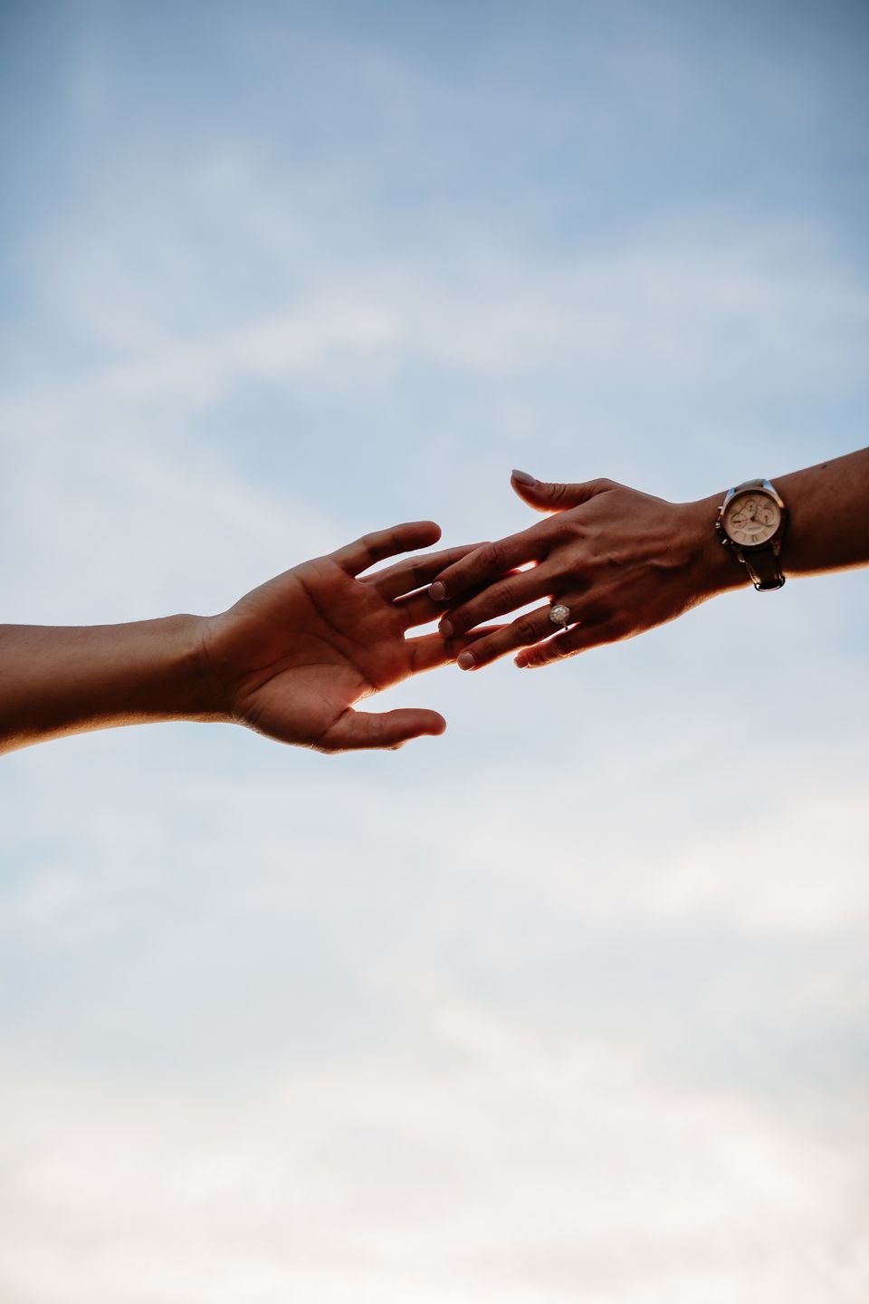 Two hands reaching toward each other against a blue sky background.