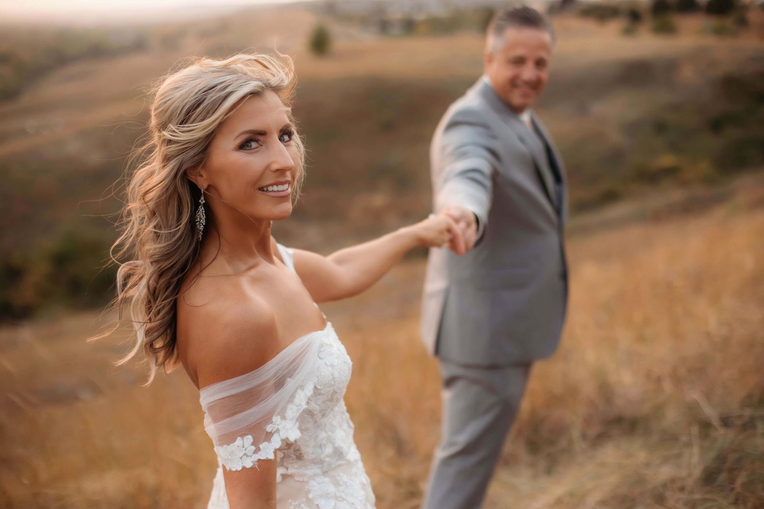 A couple in wedding attire shares a playful moment on a hilltop during their sunset photoshoot.