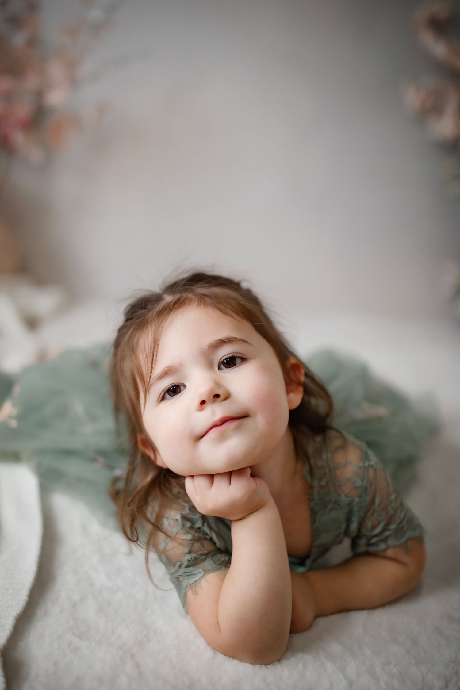 A tender portrait showing a sage green lace dress while resting on white fabric.