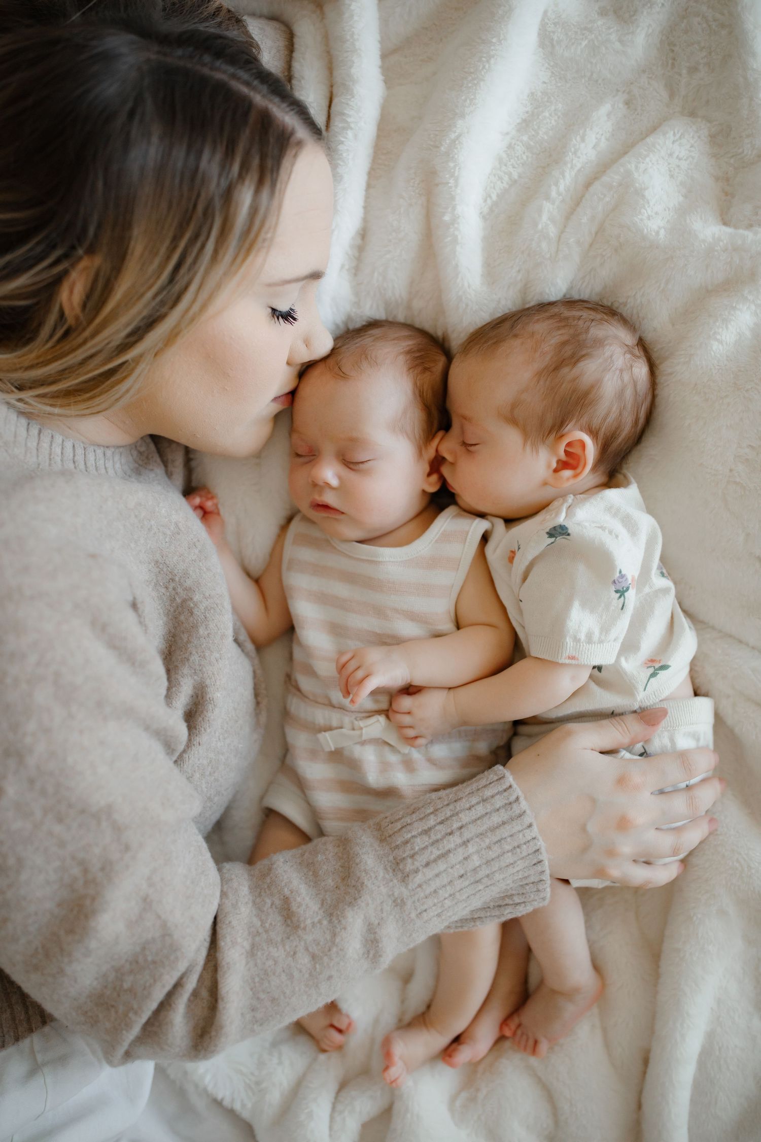 Tender family moment captured on white bedding with sleeping infants.