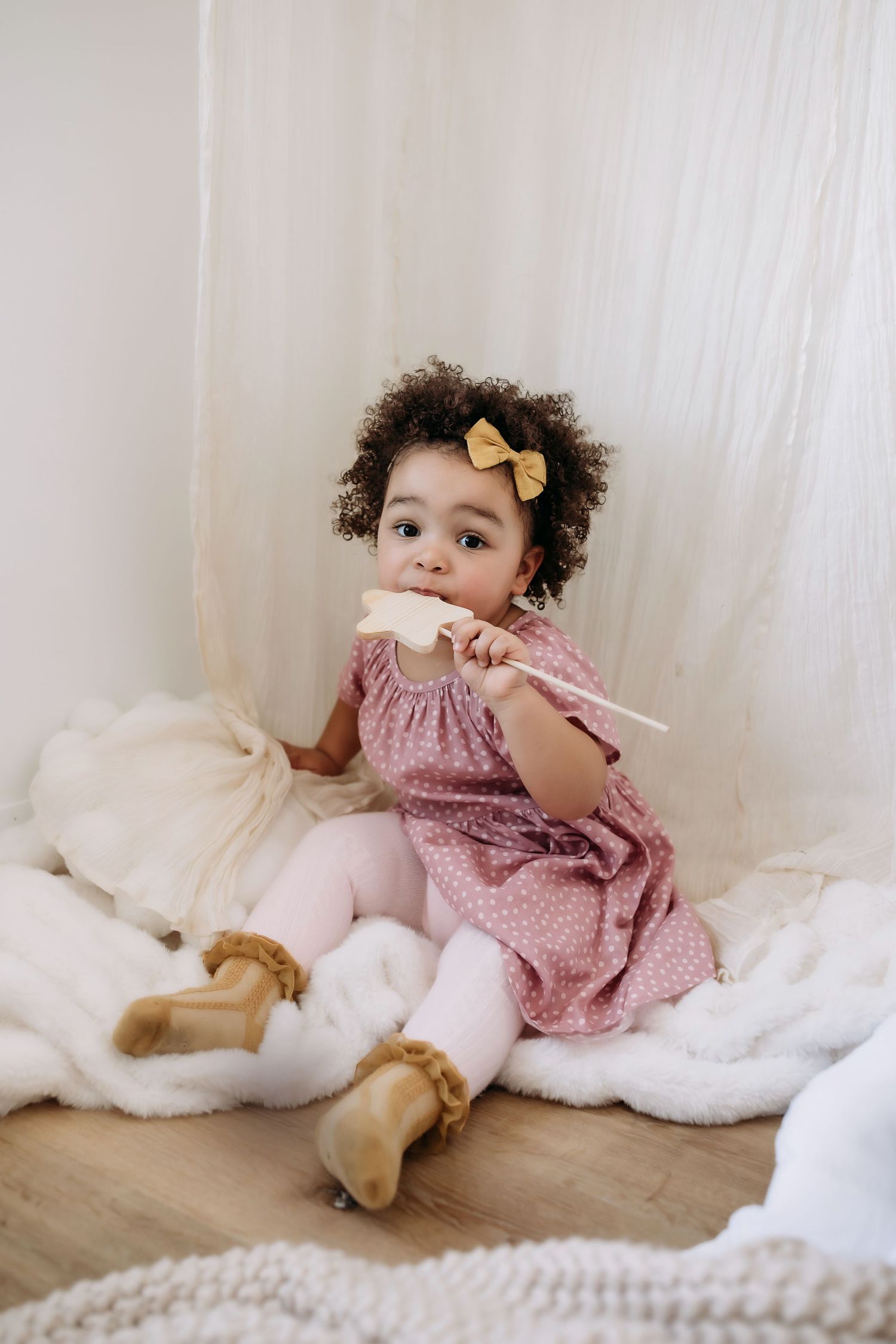 A child in pink dress plays with toys while sitting on white blankets.