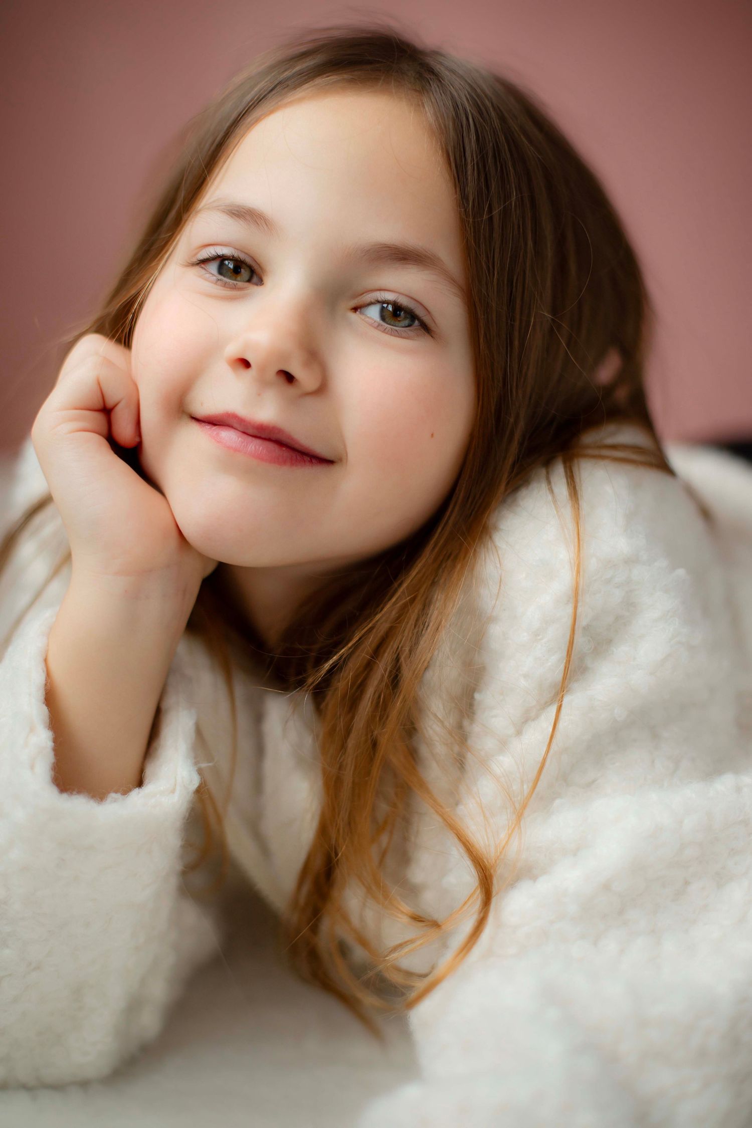 Portrait series showing gentle expressions and soft white sweater against a warm pink background.