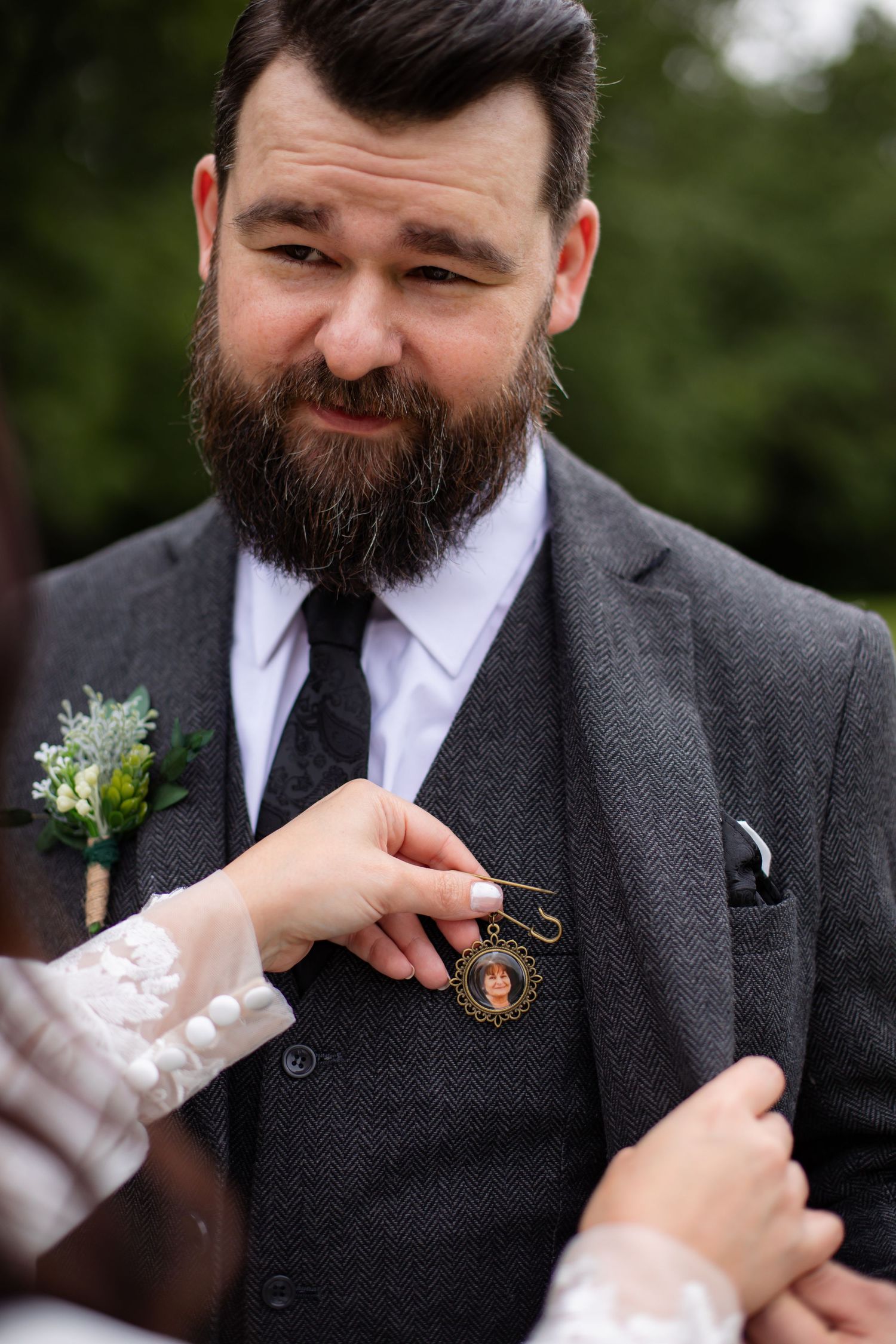 A boutonniere being pinned onto a grey suit jacket during wedding preparations.